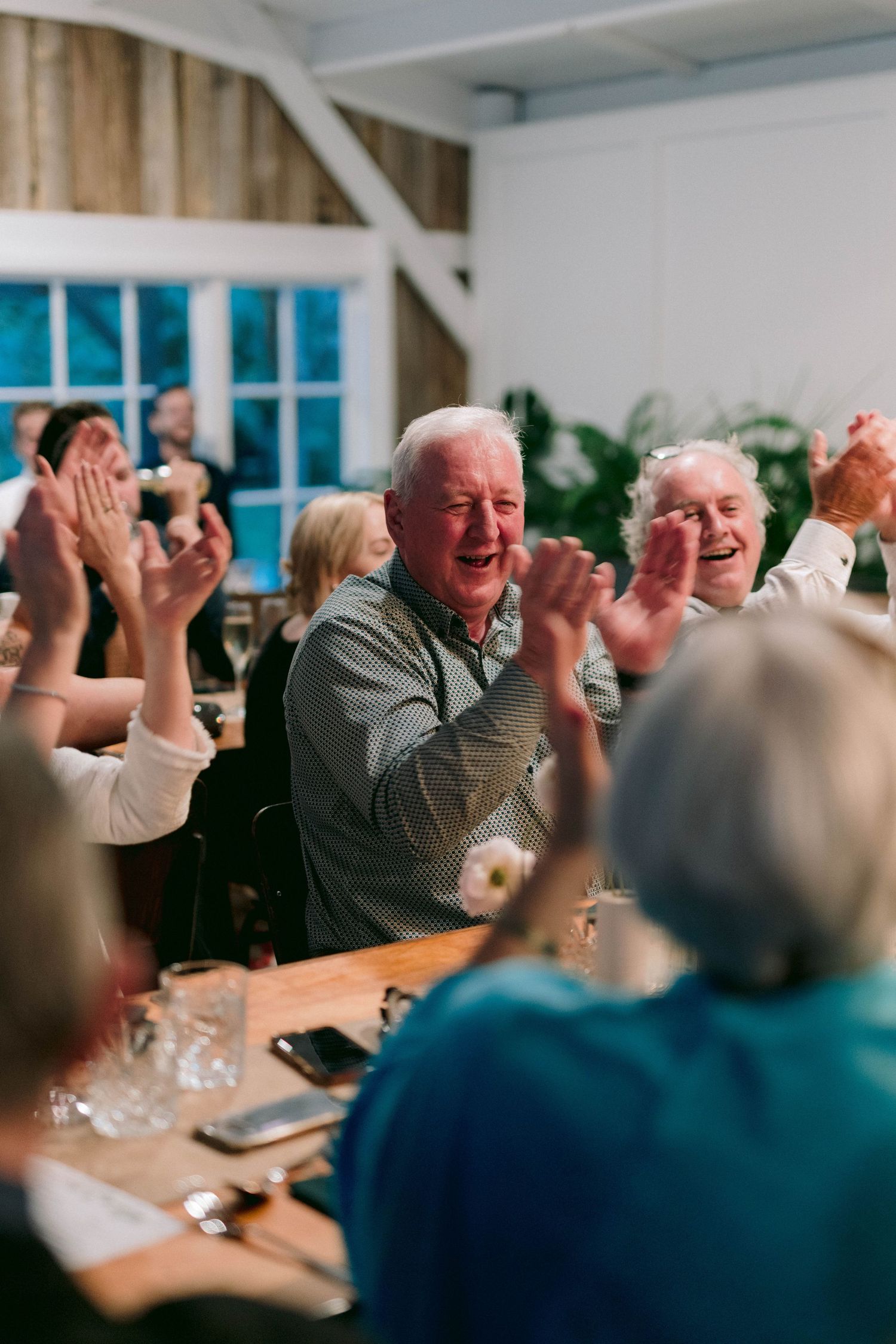 People clapping and celebrating during a festive gathering at a dining table.