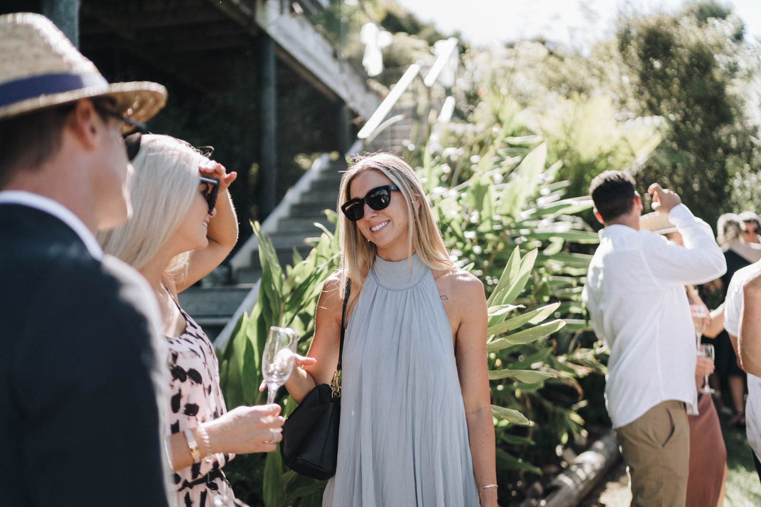 A group of people enjoying a sunny outdoor gathering with lush greenery and foliage in the background.