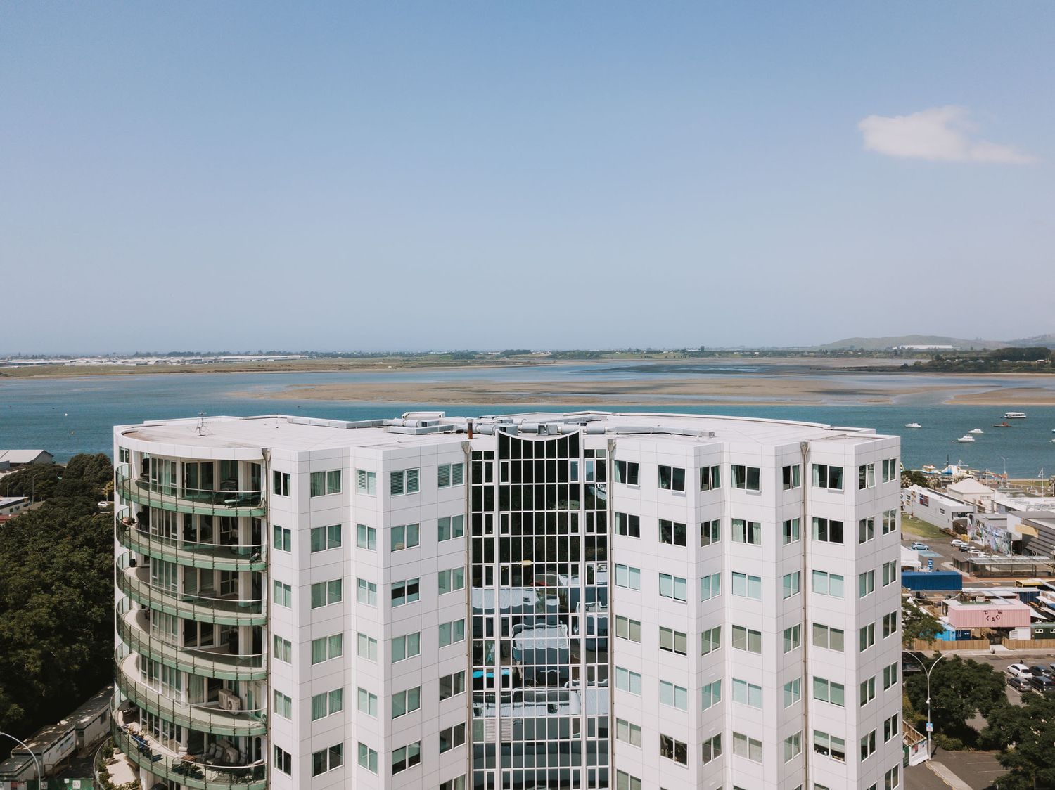 Modern oceanfront apartment building with curved white balconies and glass windows overlooking coastal waters and beaches.