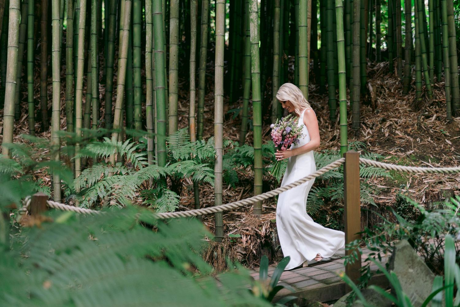 A bride in an elegant white dress poses in a serene bamboo forest setting.