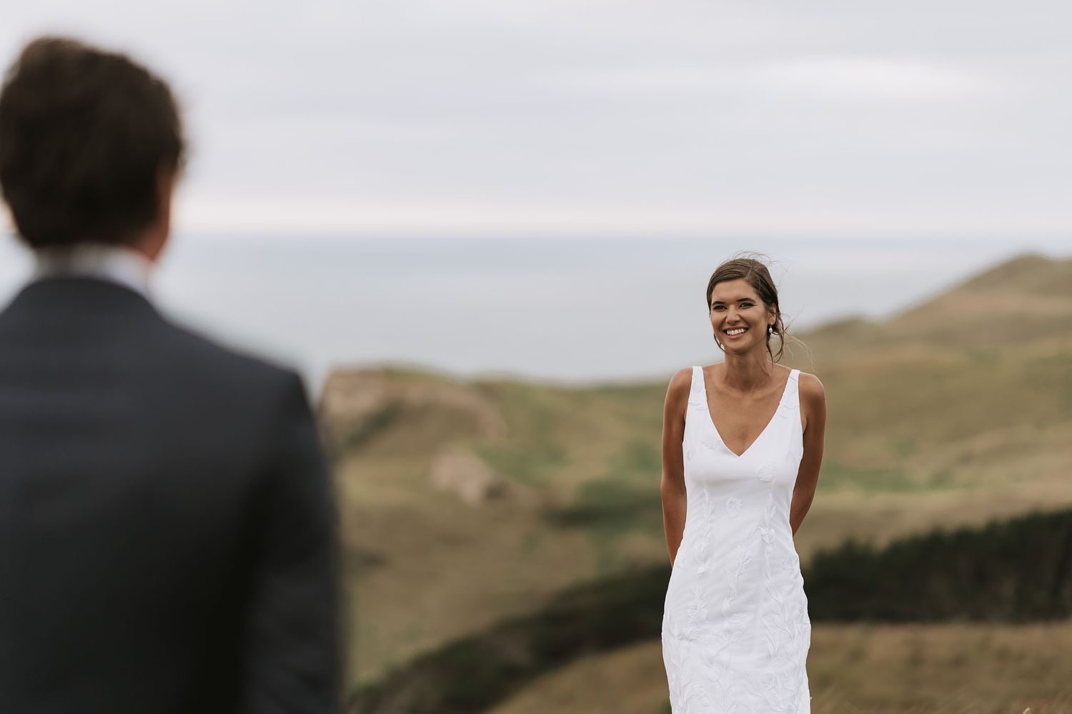 Bride and groom share an intimate moment on a scenic cliffside with sweeping ocean views.