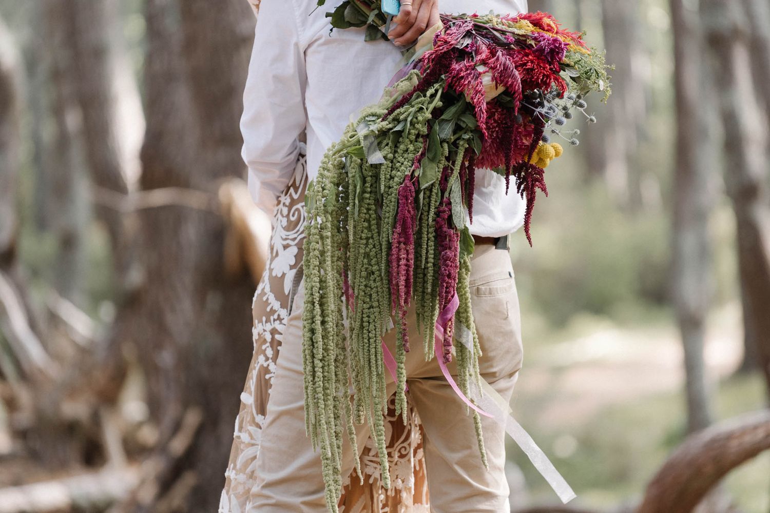 Close-up details of cascading burgundy and emerald floral wedding bouquet with trailing greenery and ribbons.