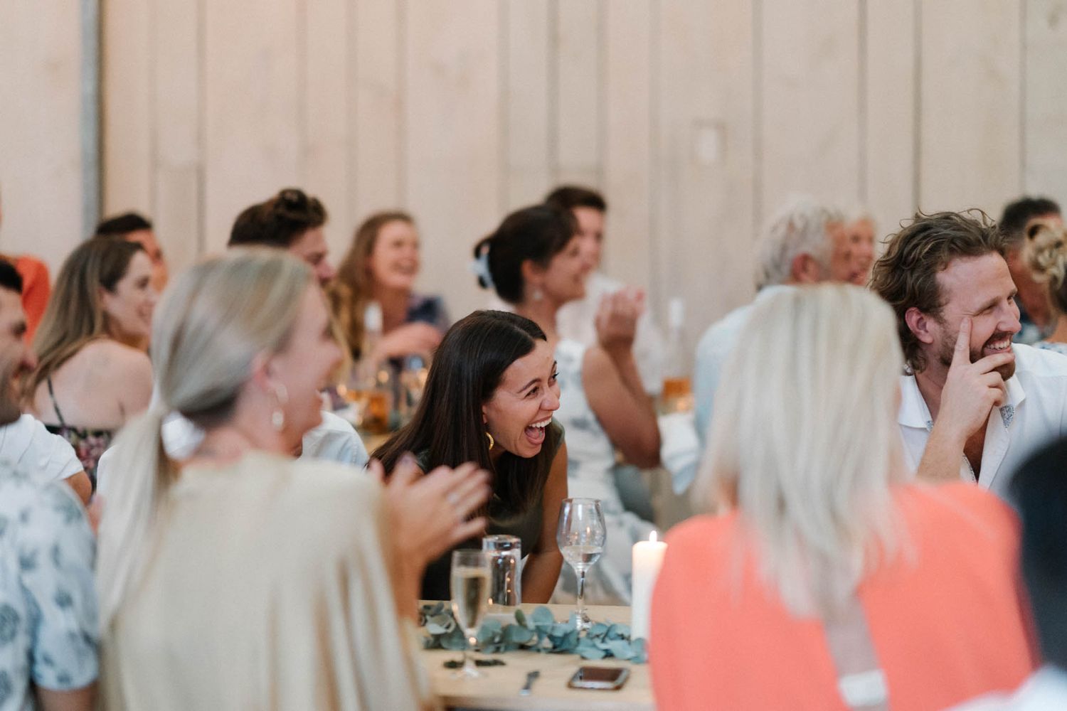 A group of wedding guests laughing and enjoying themselves at a reception dinner table.