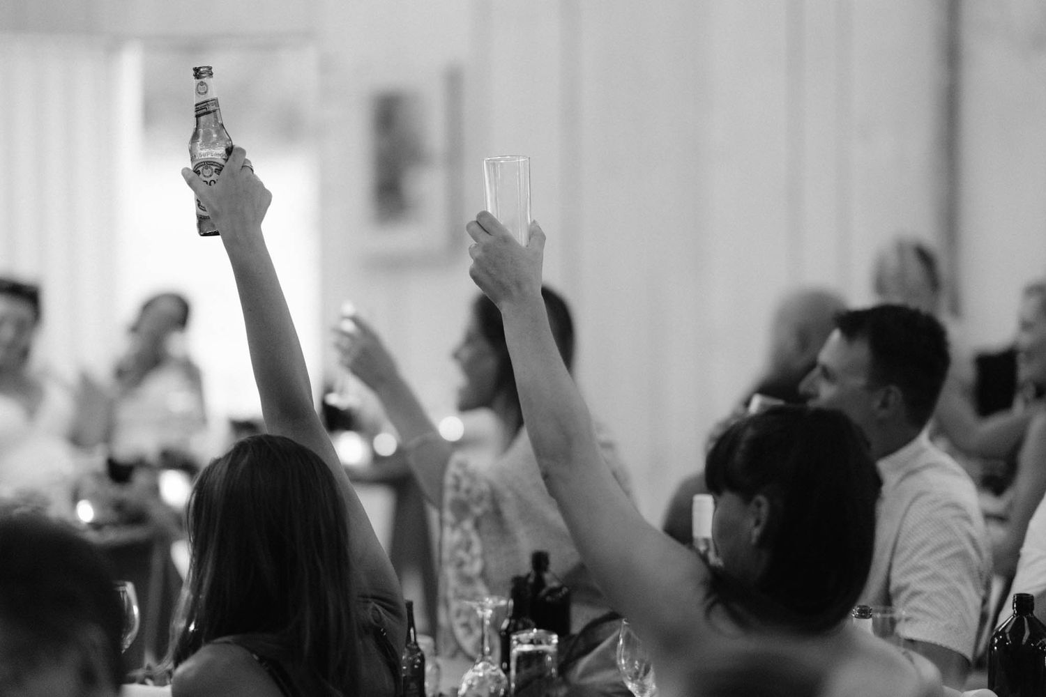 Black and white shot of people raising their hands and drinks at a celebratory gathering.