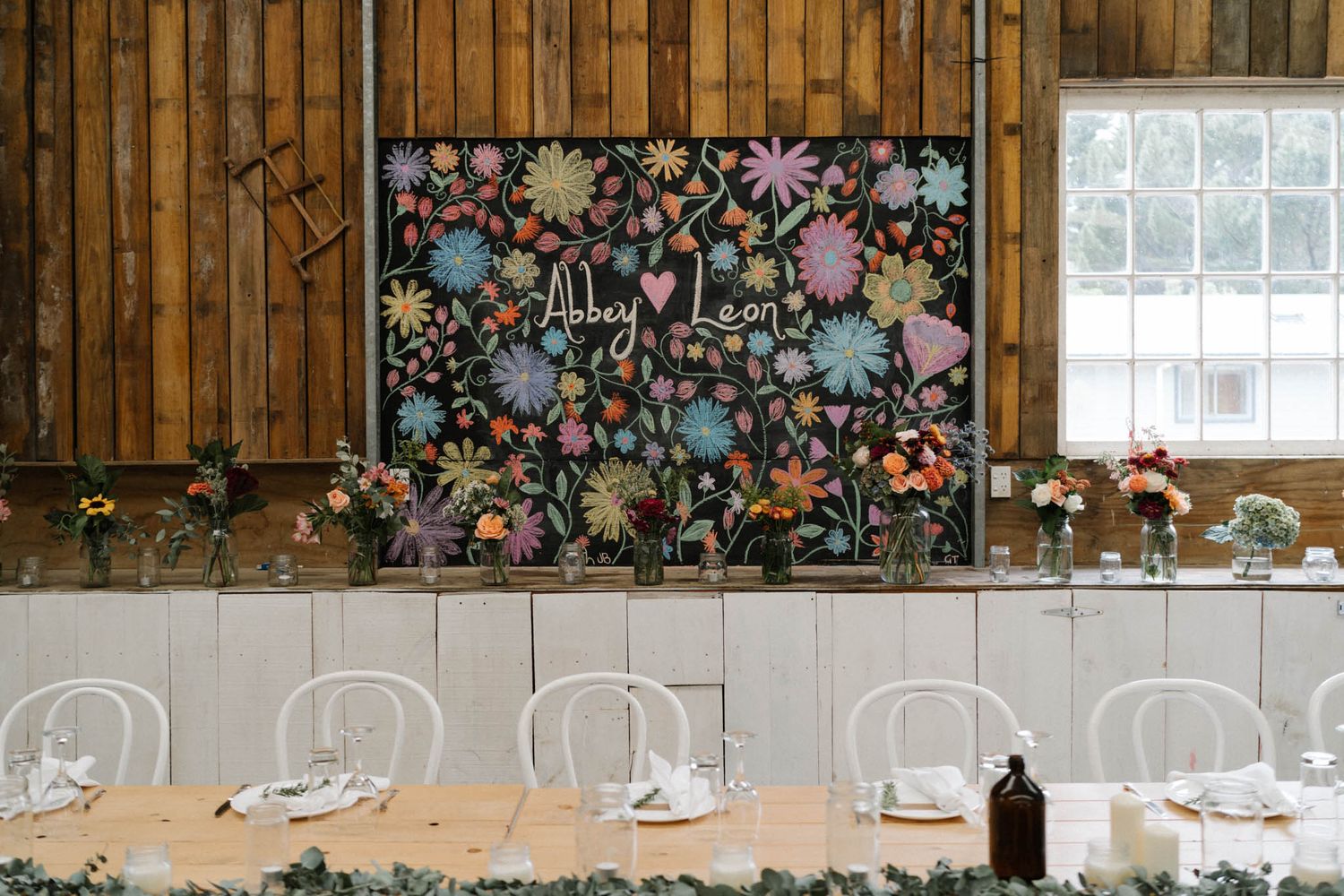 Rustic barn wedding reception venue decorated with romantic floral garlands and dangling string lights creating a warm ambiance.