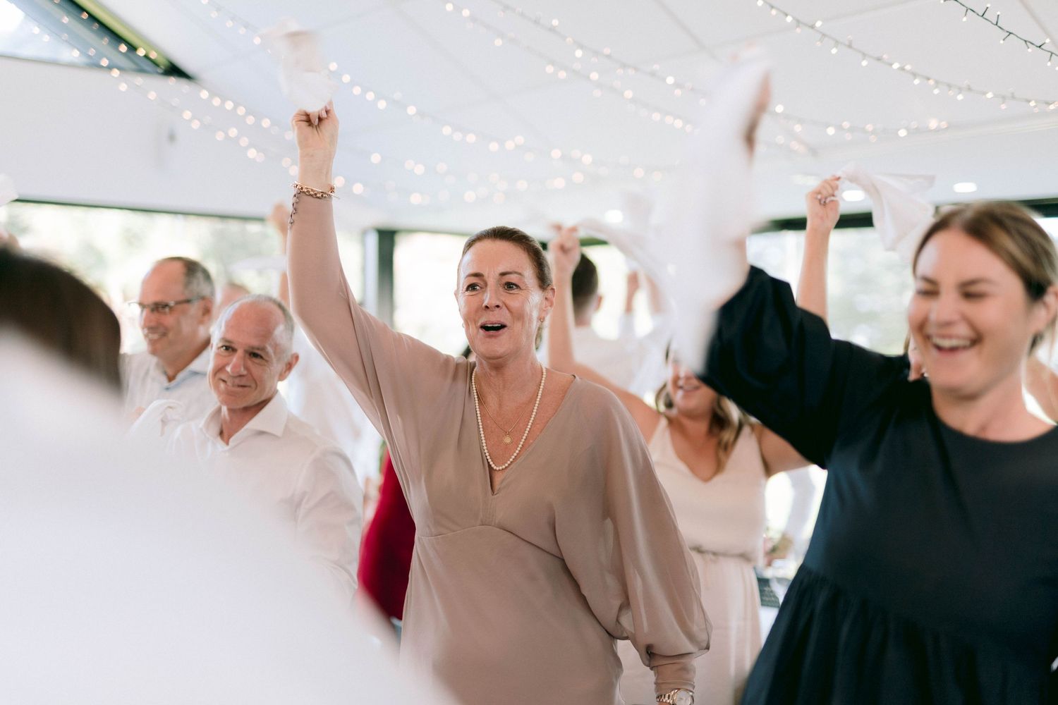 Wedding celebration with guests dancing under string lights and white party decorations.