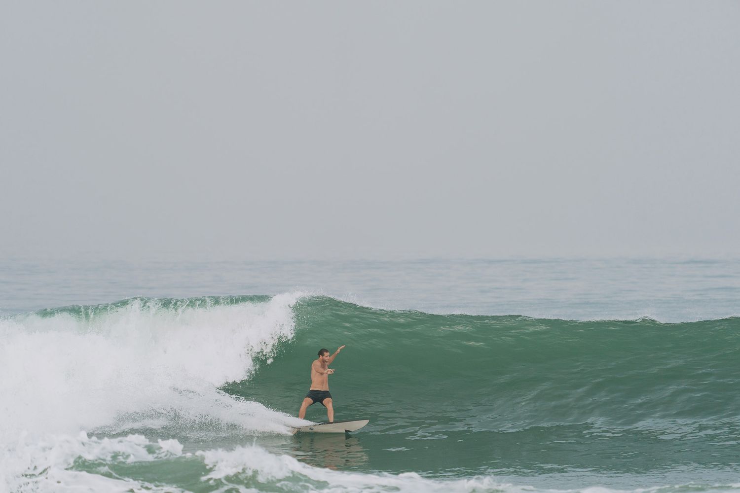 A surfer rides a green wave as white foam sprays behind them during an energetic surfing session.