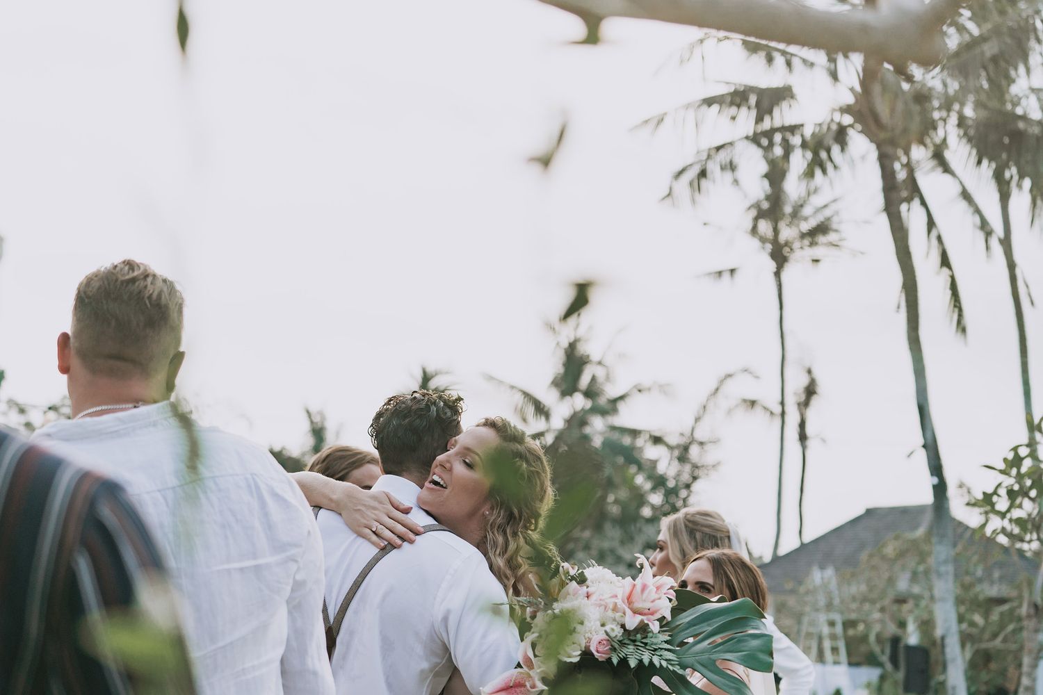 Wedding party dancing and laughing together on an outdoor patio surrounded by tropical landscaping.