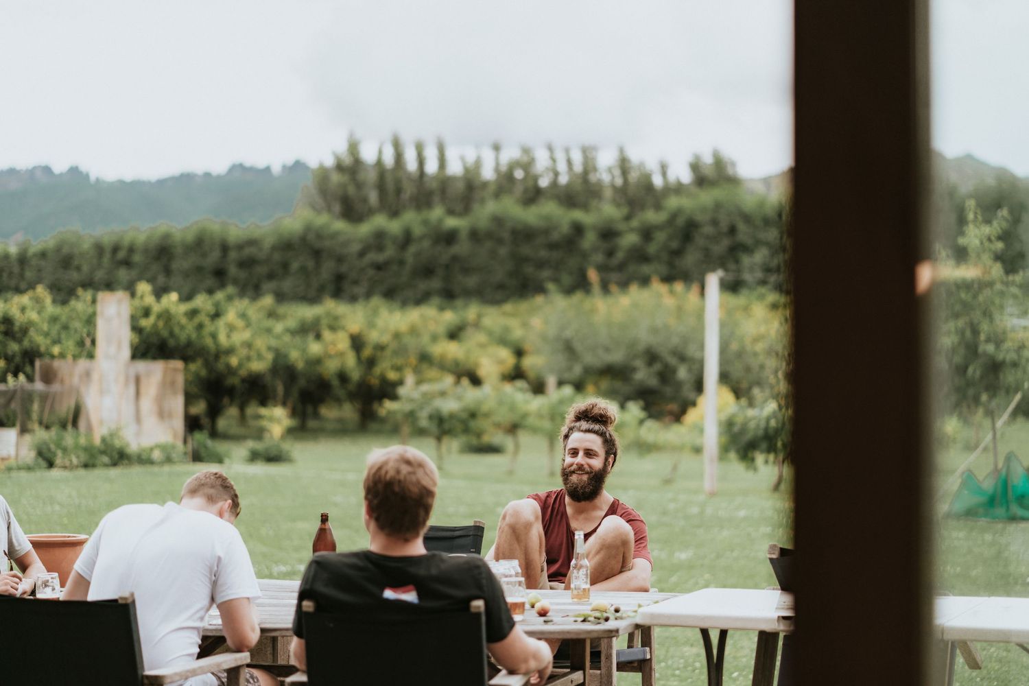 Group enjoying a casual outdoor gathering at long tables with lush green countryside and trees in the background.