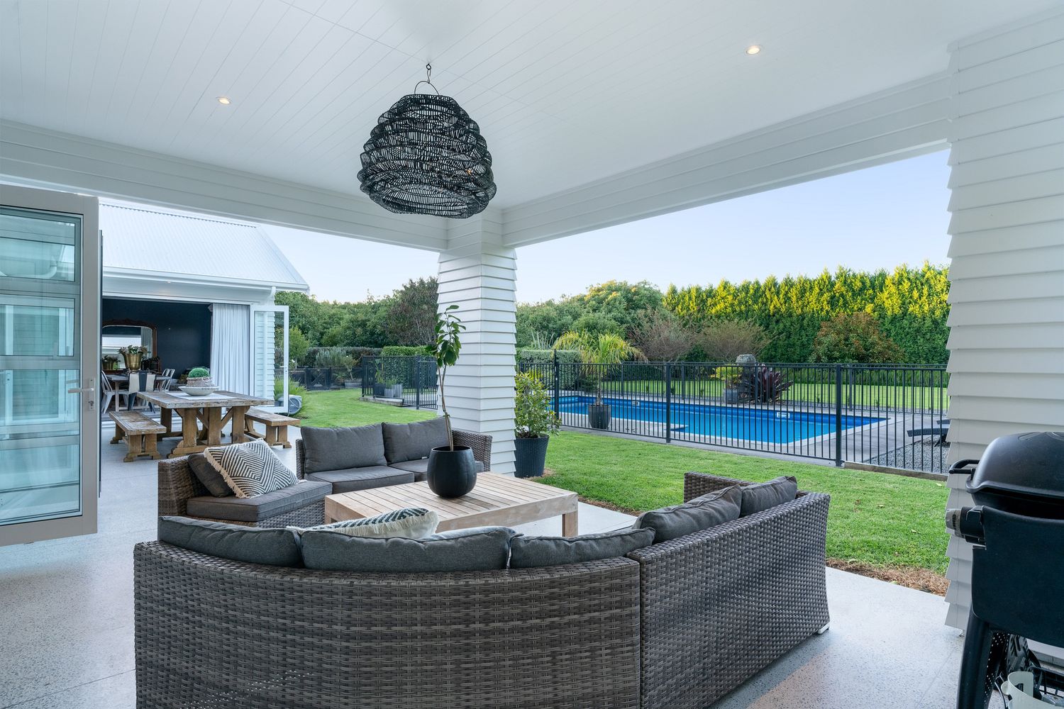 Covered outdoor living area with gray sectional sofa overlooking pool and backyard.