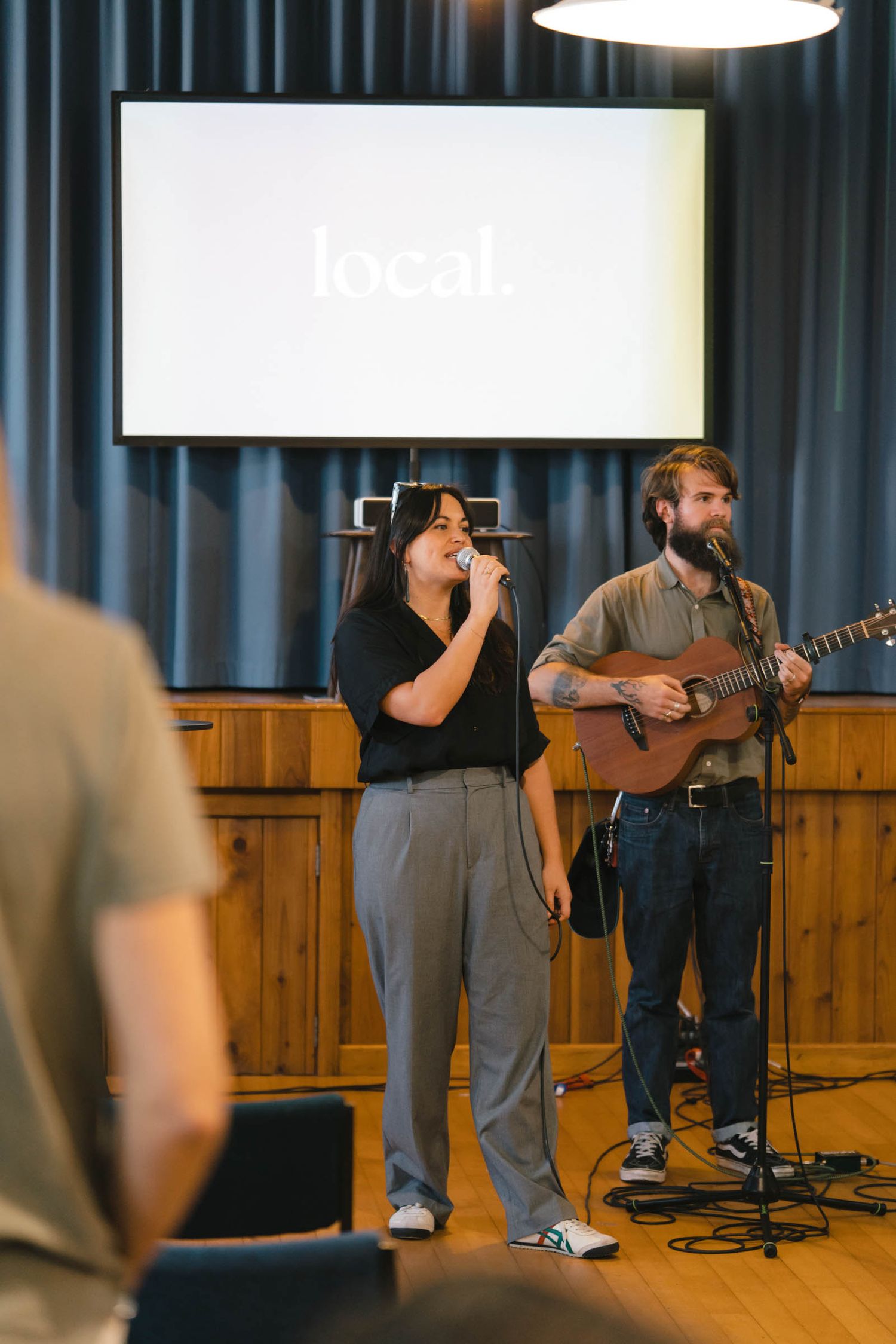 Musicians performing on stage with acoustic guitar and microphone at a church service.