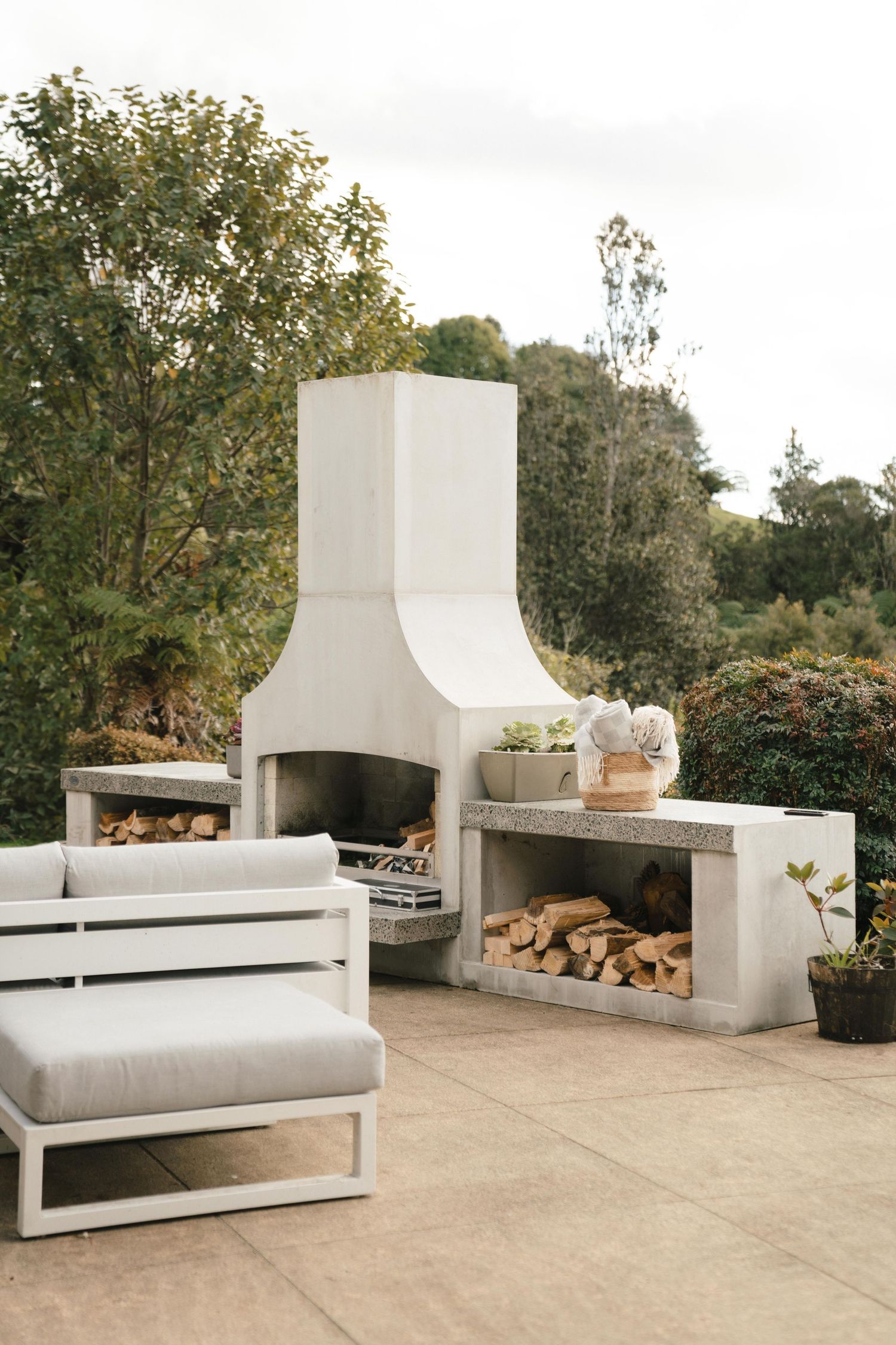 Modern white concrete outdoor patio fireplace with built-in seating and wood storage space in minimalist design.