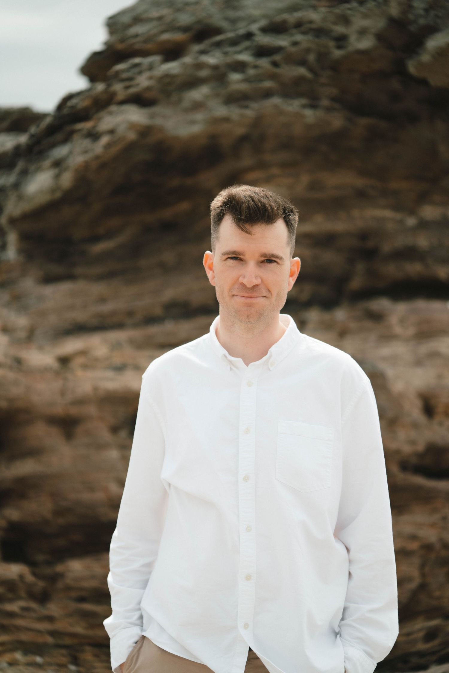 Person in crisp white button-down shirt poses against rugged coastal rock formations.