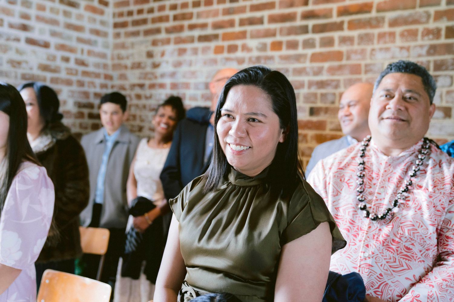 Wedding guests seated in rows at indoor ceremony with brick walls.