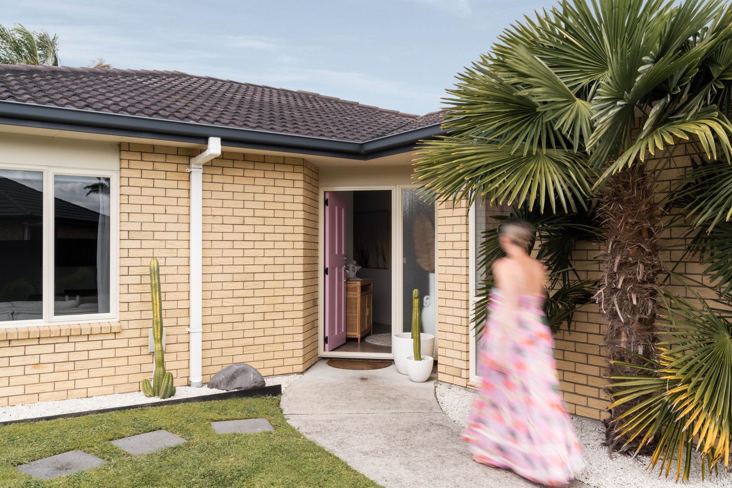 A modern beige brick home with palm trees and a walkway leading to the front entrance.