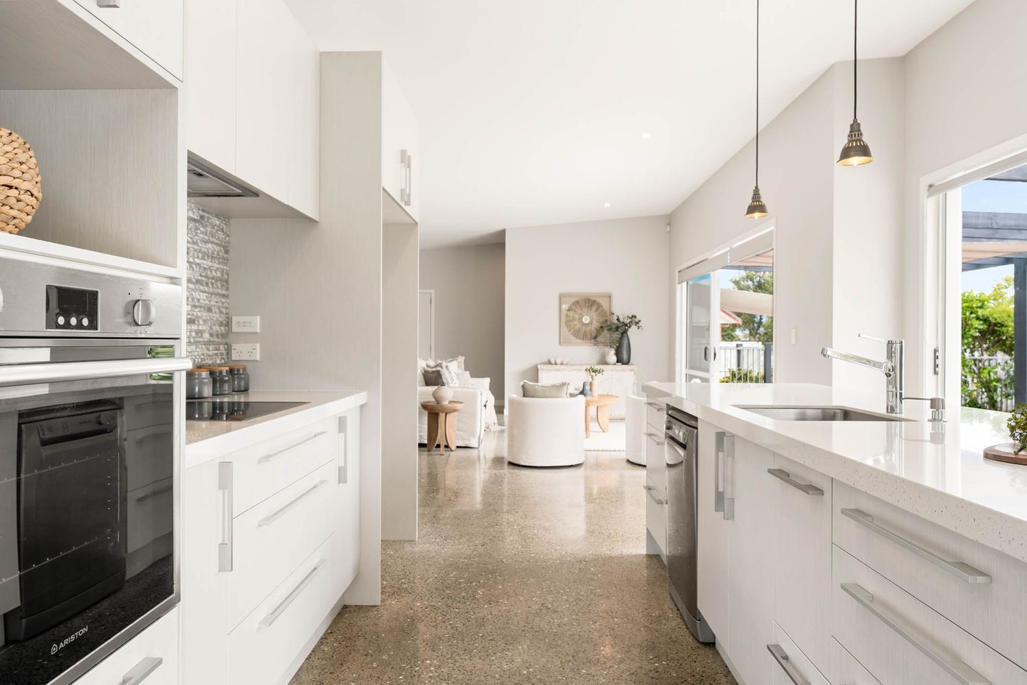 Modern white kitchen with polished concrete floors and pendant lights opens to a bright living area.