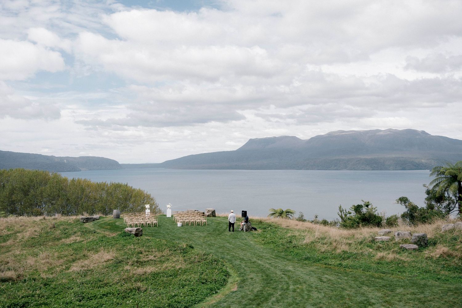 People walking on a grassy hilltop path overlooking a scenic mountain lake.