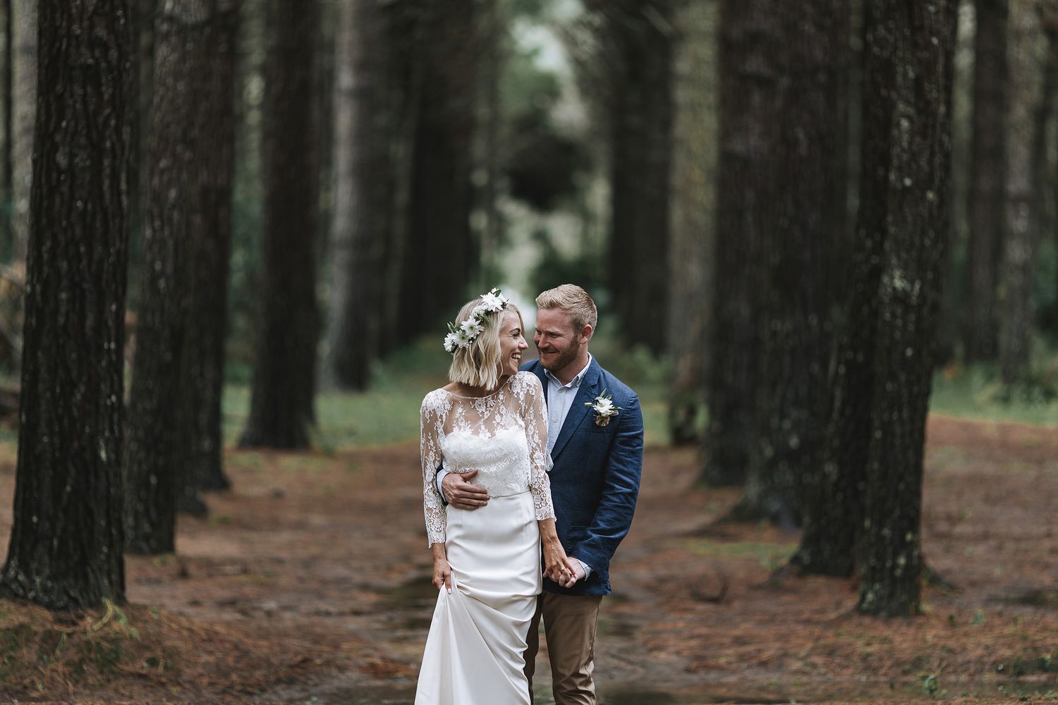 A romantic wedding photo of a couple sharing a joyful moment together in a serene pine forest setting.