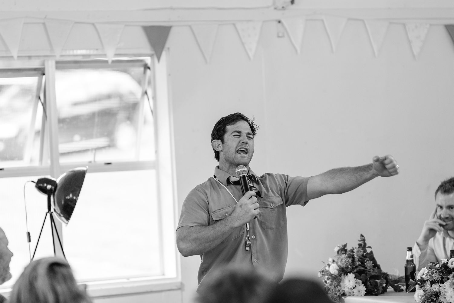 A speaker at an informal gathering gestures enthusiastically while addressing the audience in a room with bunting decorations.
