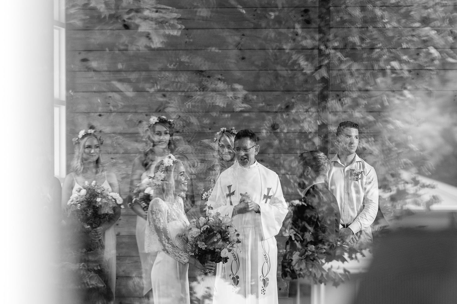 Wedding party stands for a monochromatic portrait on a spacious lawn in front of a rustic stone wall.