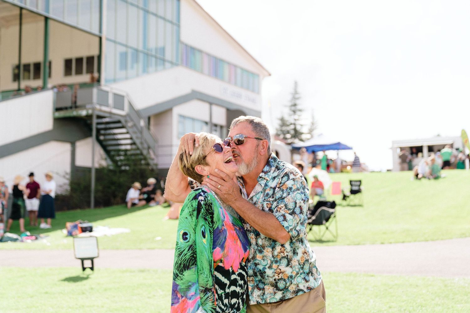 Couple sharing an intimate moment on a grassy lawn outside a modern building.