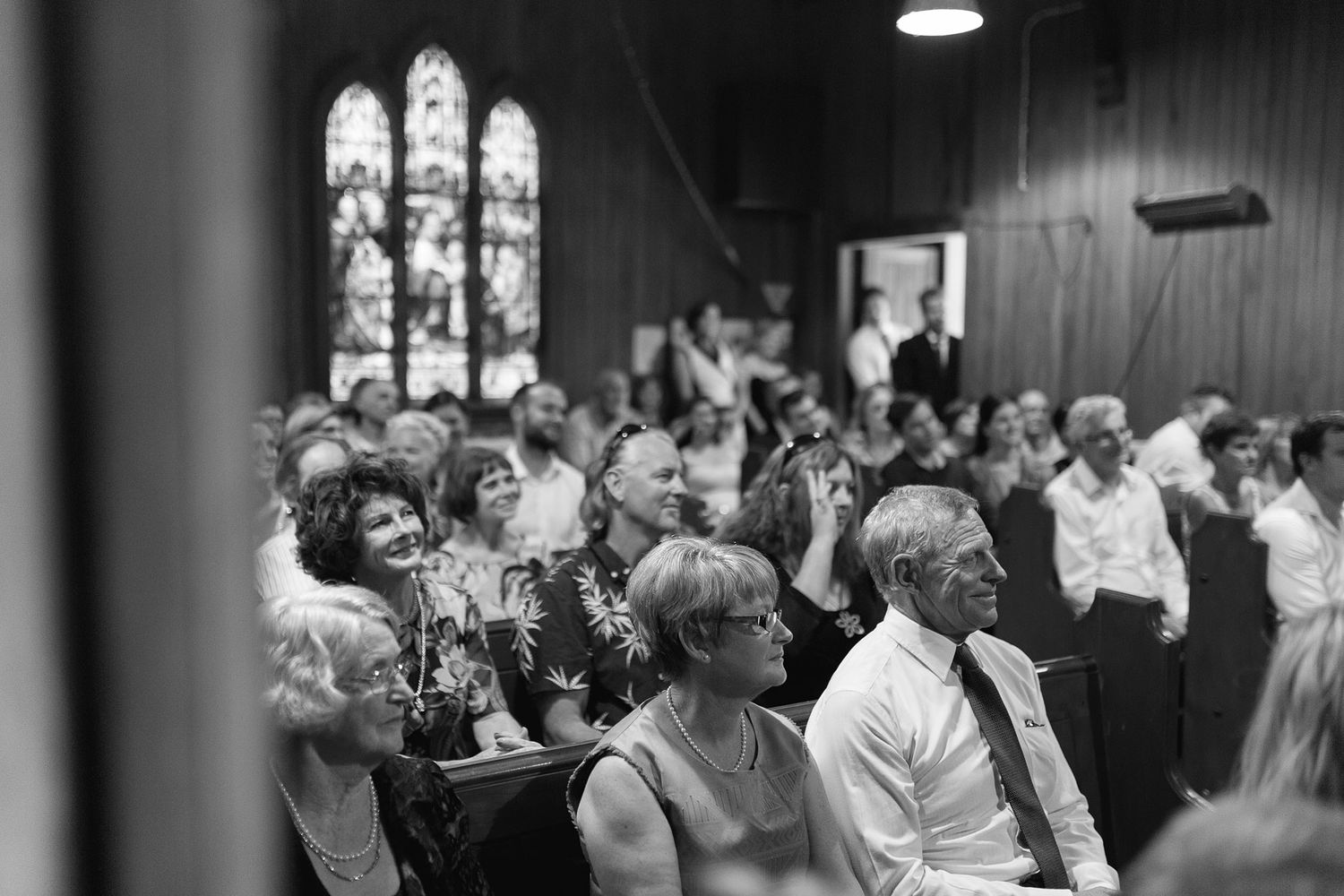 A black and white photo of a church congregation laughing together during a service as light streams through stained glass windows.