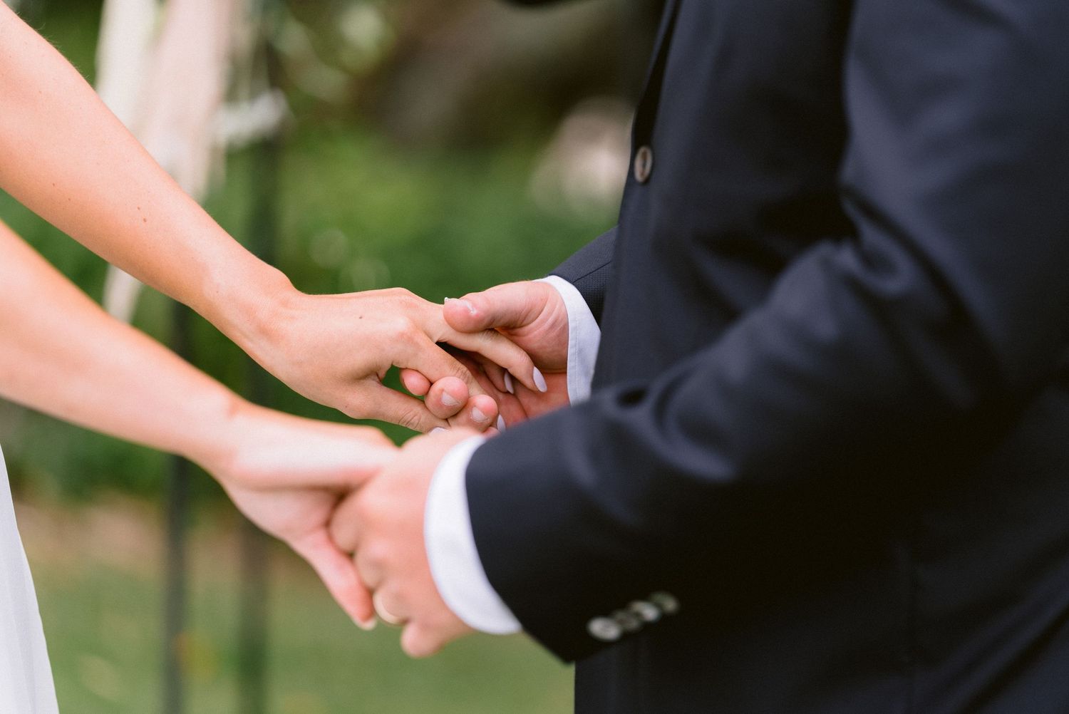 Close-up of hands exchanging rings during an outdoor wedding ceremony.
