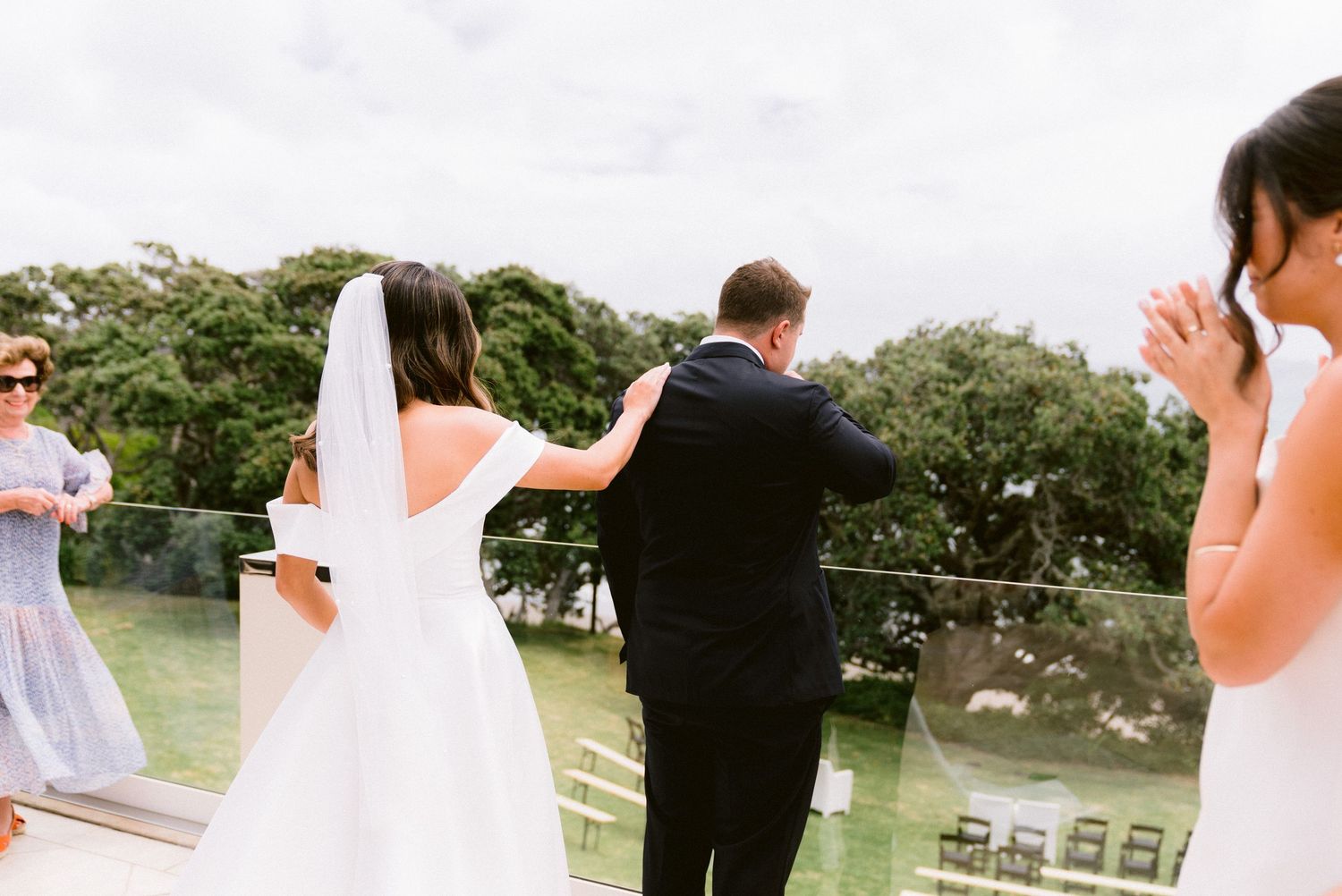 Light and airy wedding ceremony setup with white chairs arranged outdoors near water.