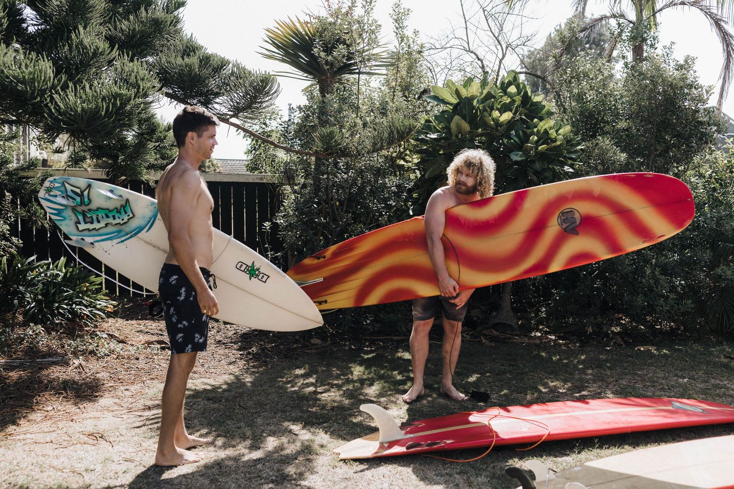 Surfboards are lined up against a wall outdoors during a sunny day.