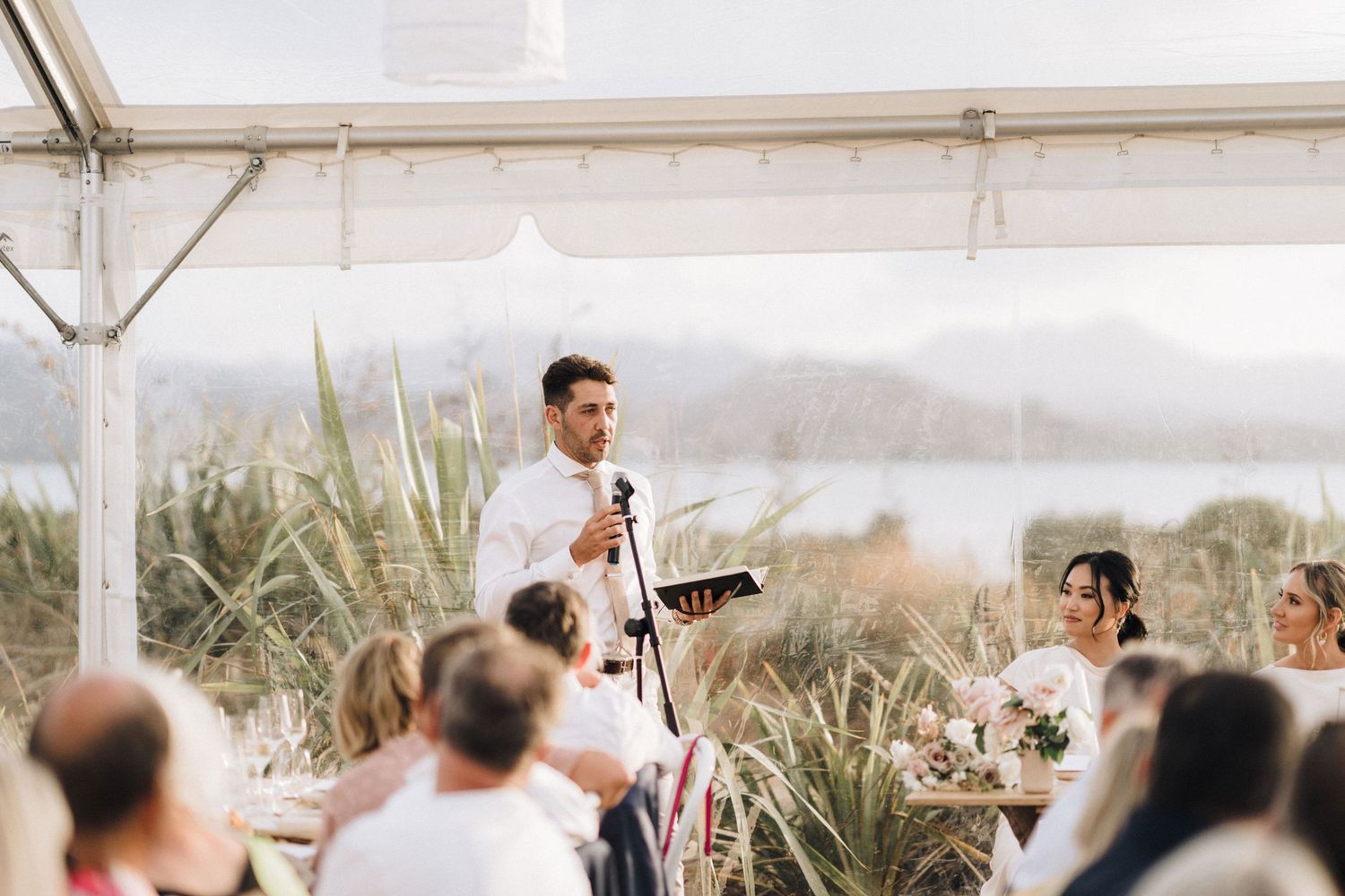 Wedding ceremony overlooking scenic ocean view with guests watching under bright sky.