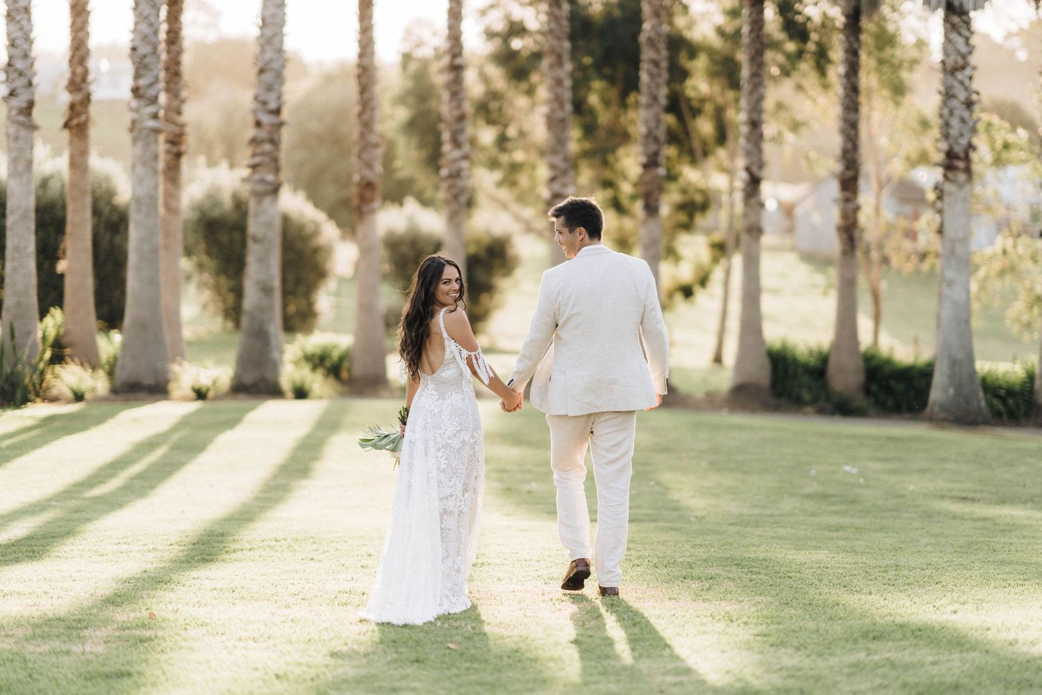 Sun-drenched pathway lined with trees creates magical setting for wedding photography session.