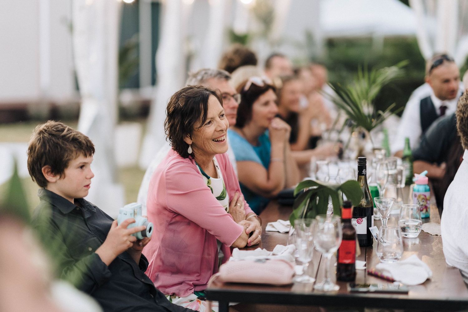 Guests seated at a long table enjoying a wedding reception meal with wine glasses and table settings.