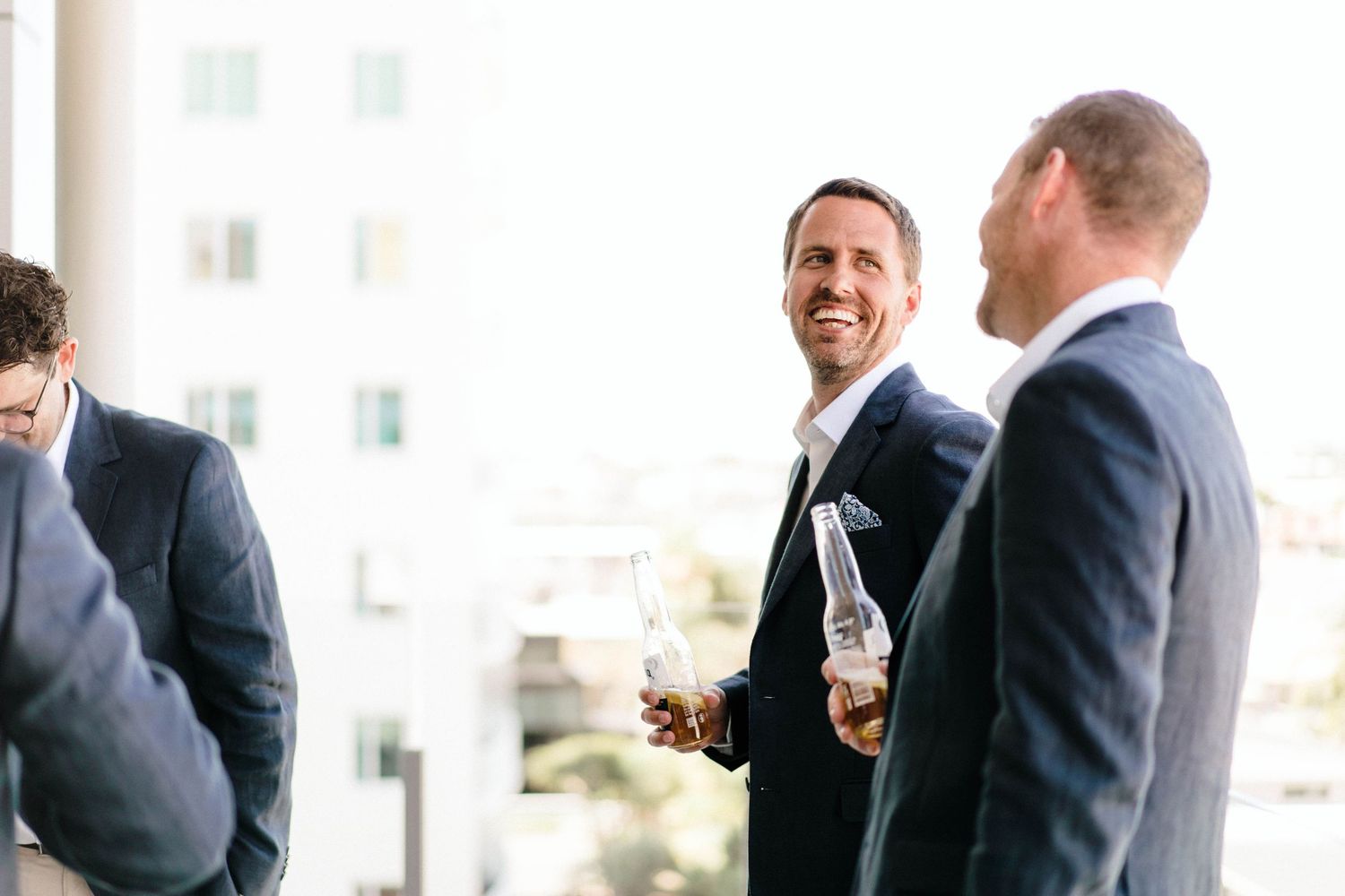 Three business professionals in suits share drinks and conversation during a casual networking event.