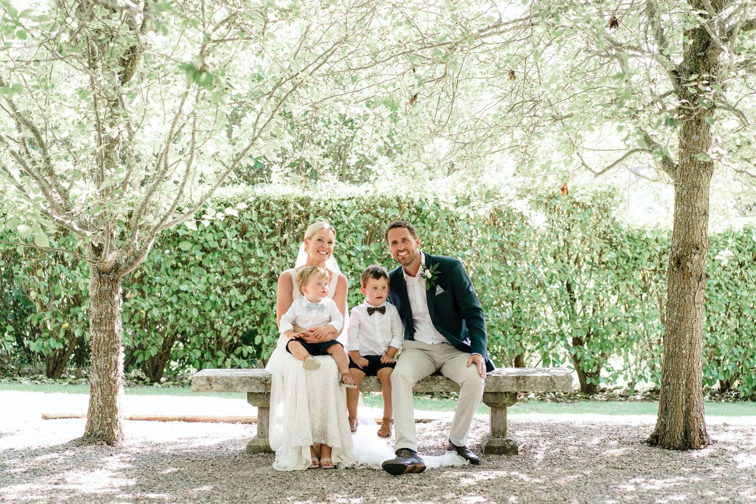 Family seated outdoors under trees during casual wedding ceremony.
