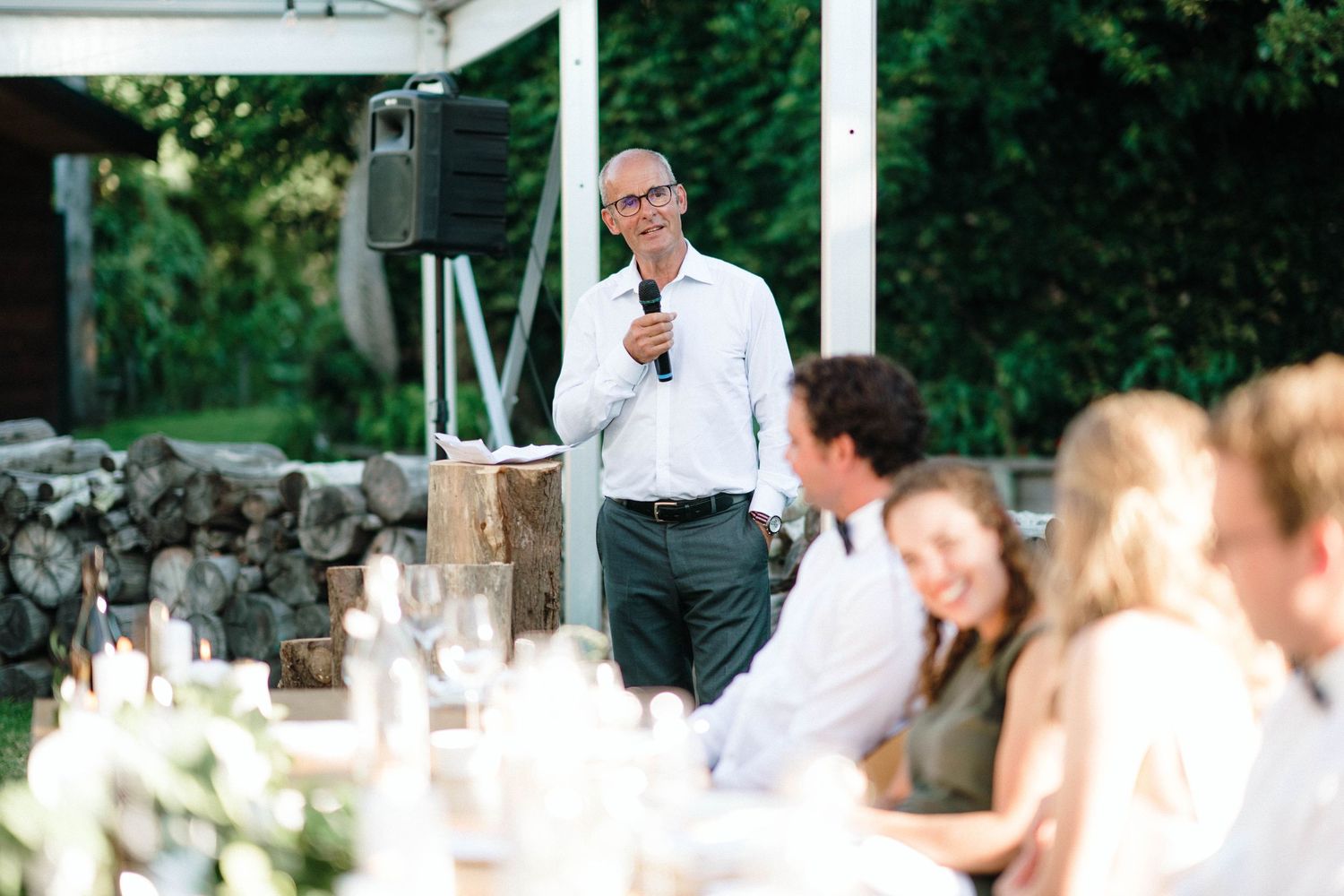 Speaker giving a toast at an elegant outdoor wedding reception with tables of guests.