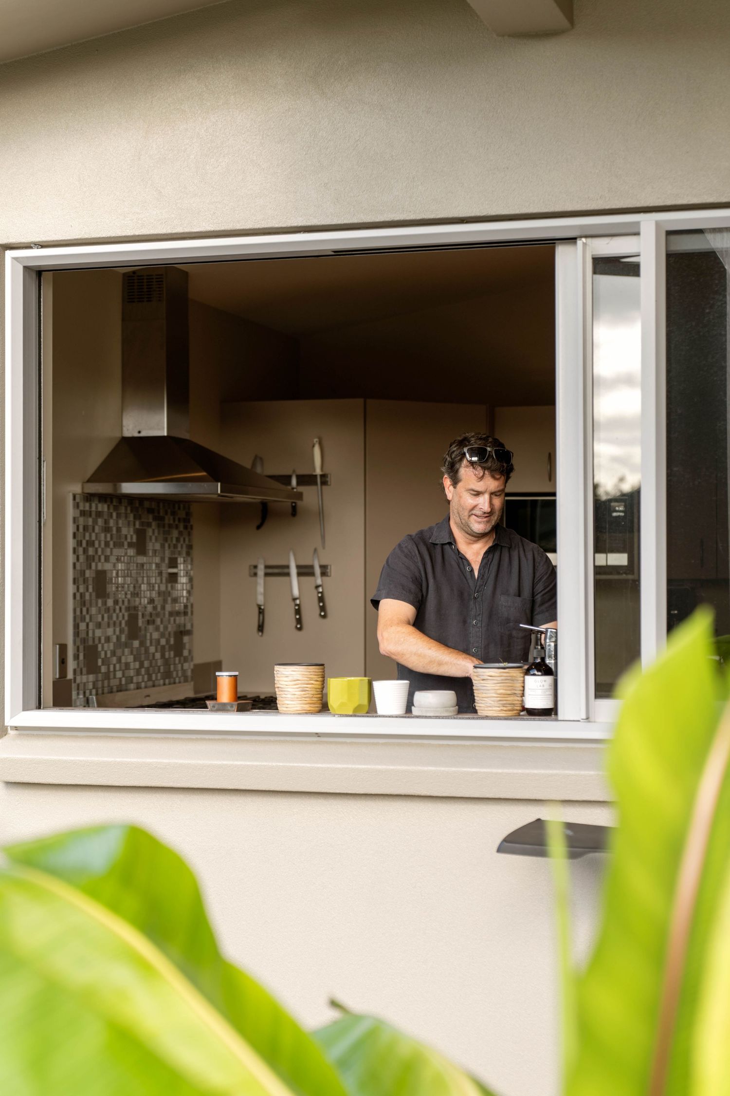 Open glass windows in a modern kitchen reveal a bright, minimalist interior space with cream-colored walls and clean lines.