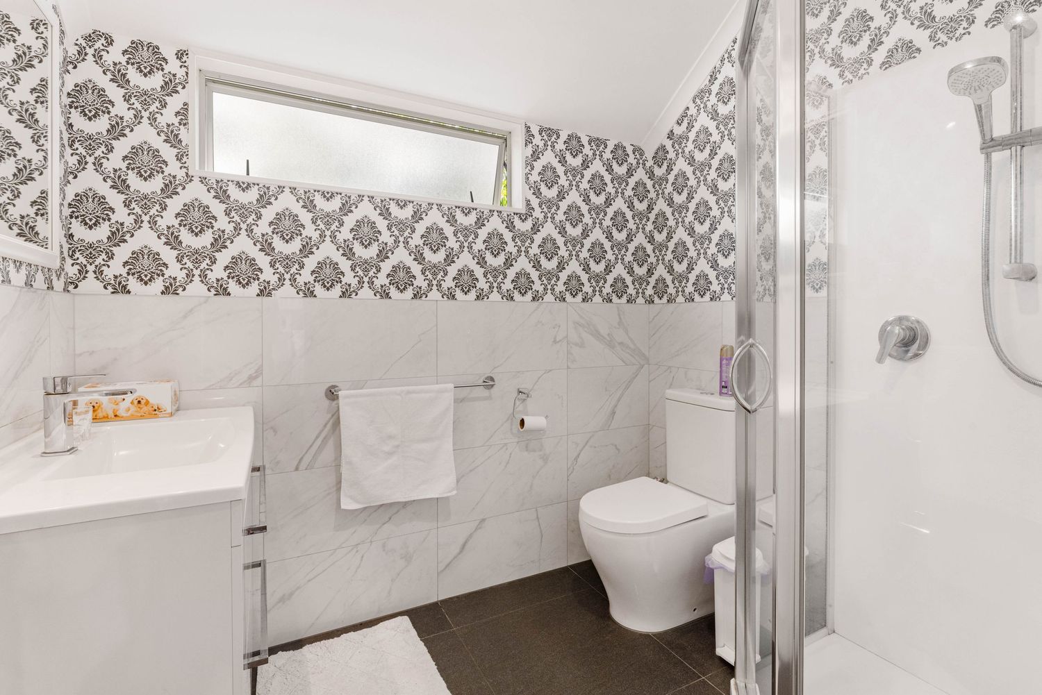 Elegant bathroom featuring patterned wallpaper, glass shower enclosure, and modern fixtures.