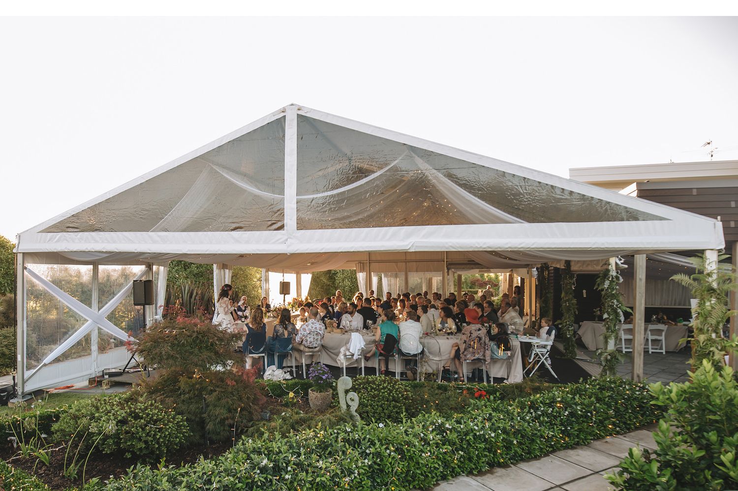 An outdoor wedding reception venue with white tents, green landscaping, and elegant table settings.