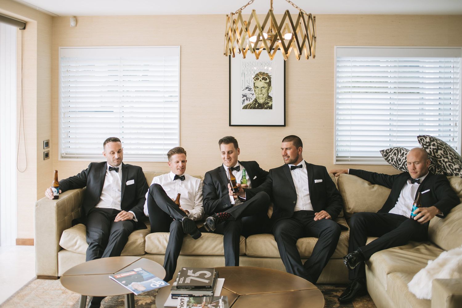 A group of people in formal suits sit together on a cream-colored couch in a bright living room interior.