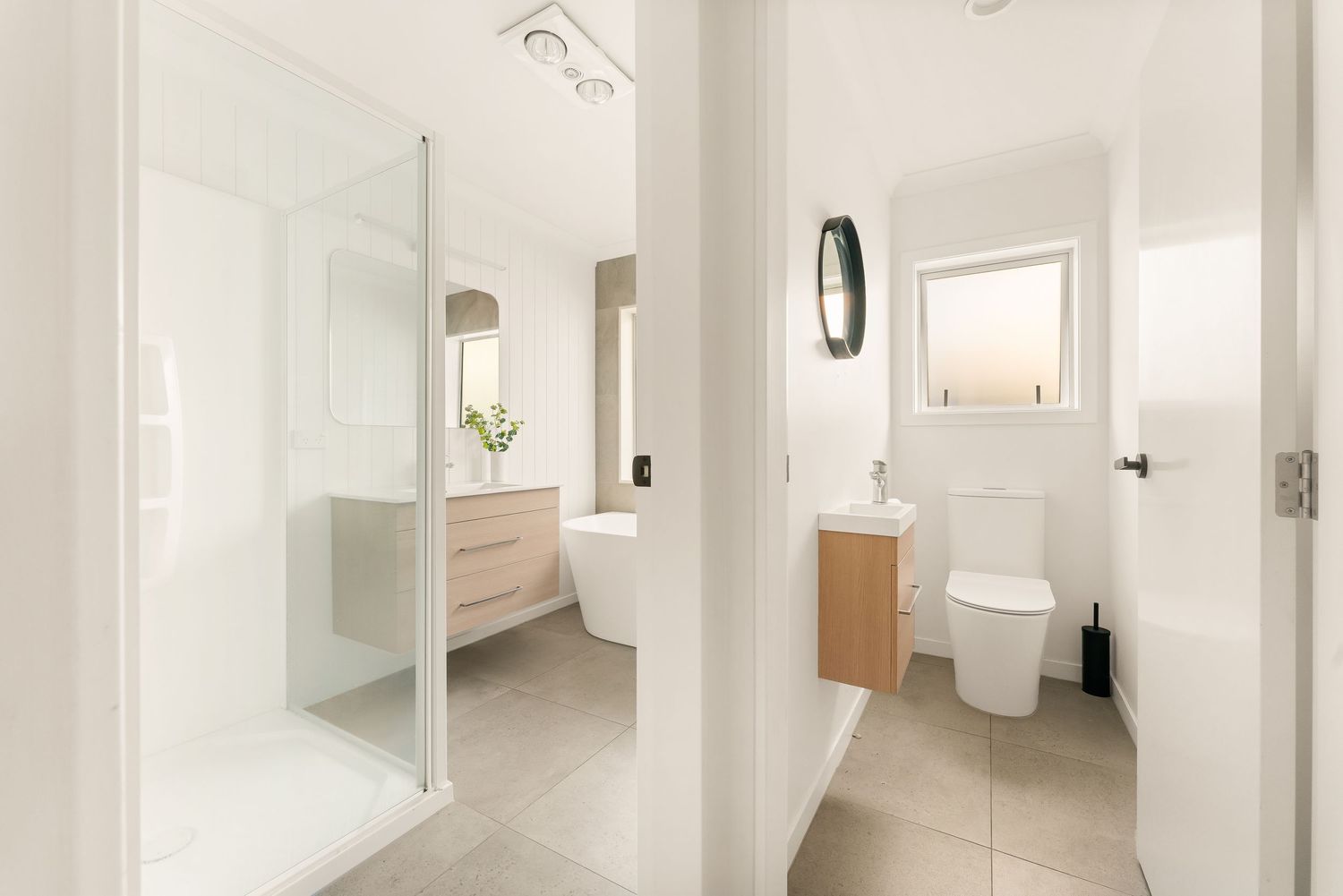 Modern white bathroom interior with glass shower enclosure, wooden vanity, and minimalist toilet room design.