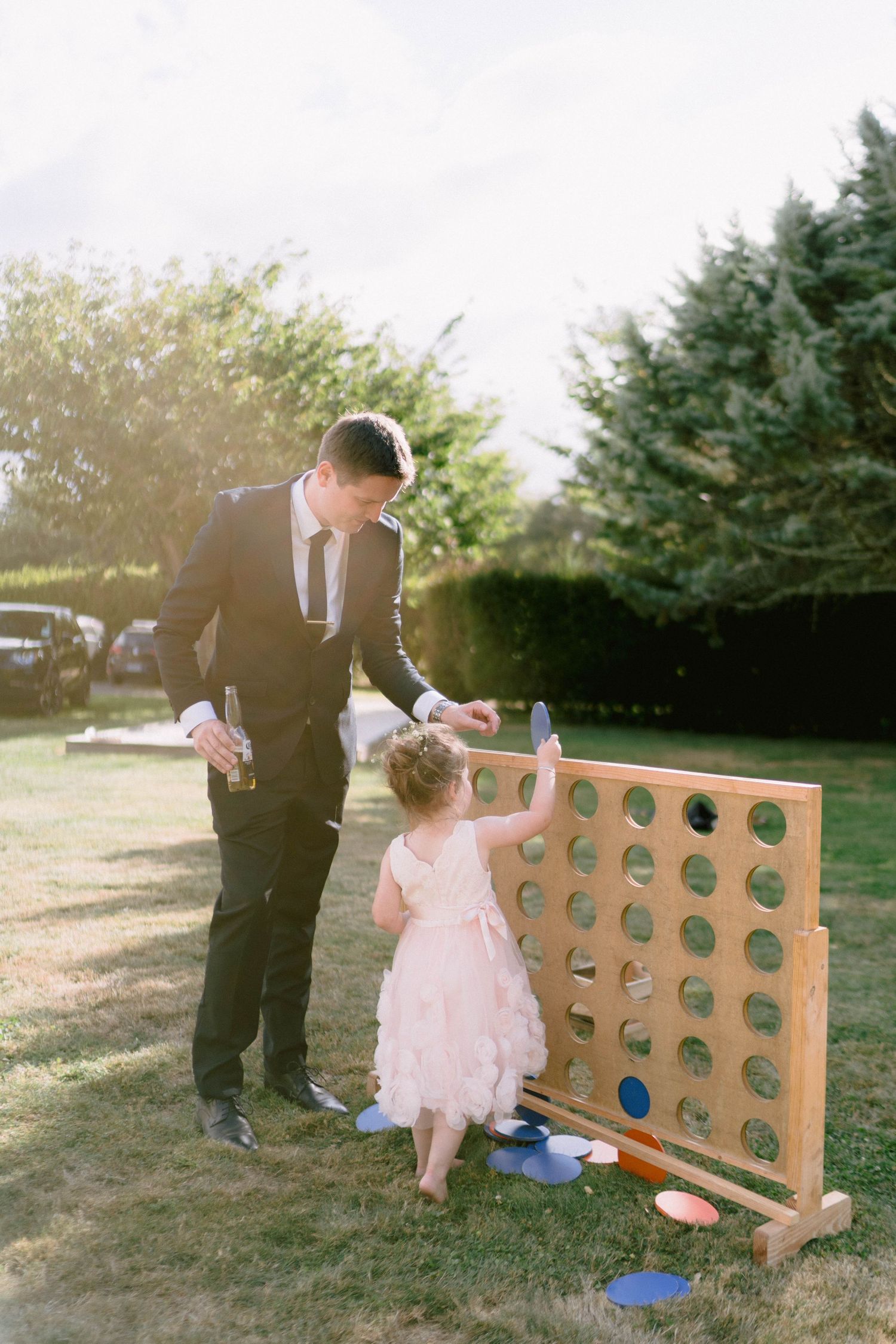 People playing a large wooden Connect Four game on a lawn during a wedding reception.