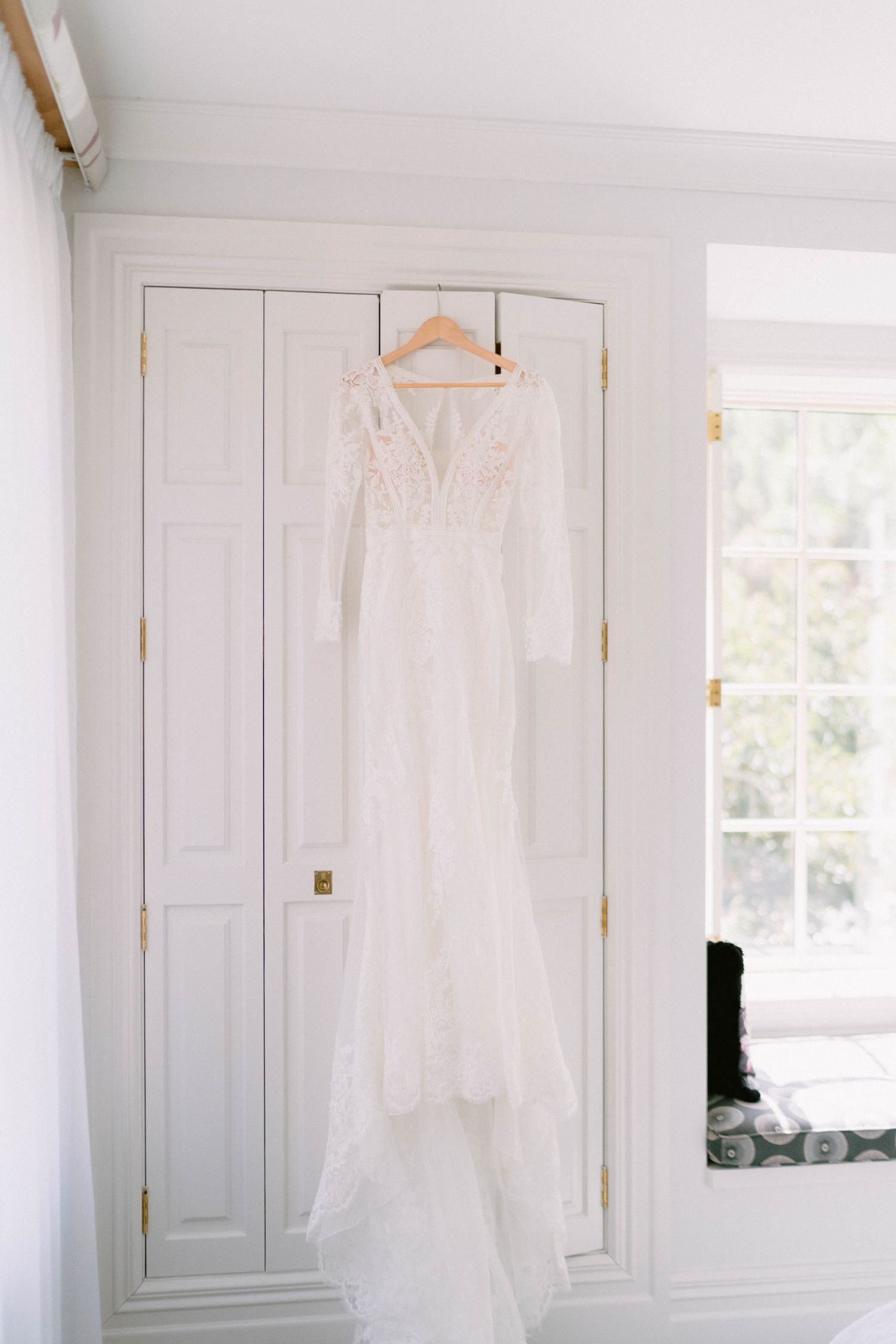 Three elegant white wedding dresses hanging on wooden hangers against white closet doors.