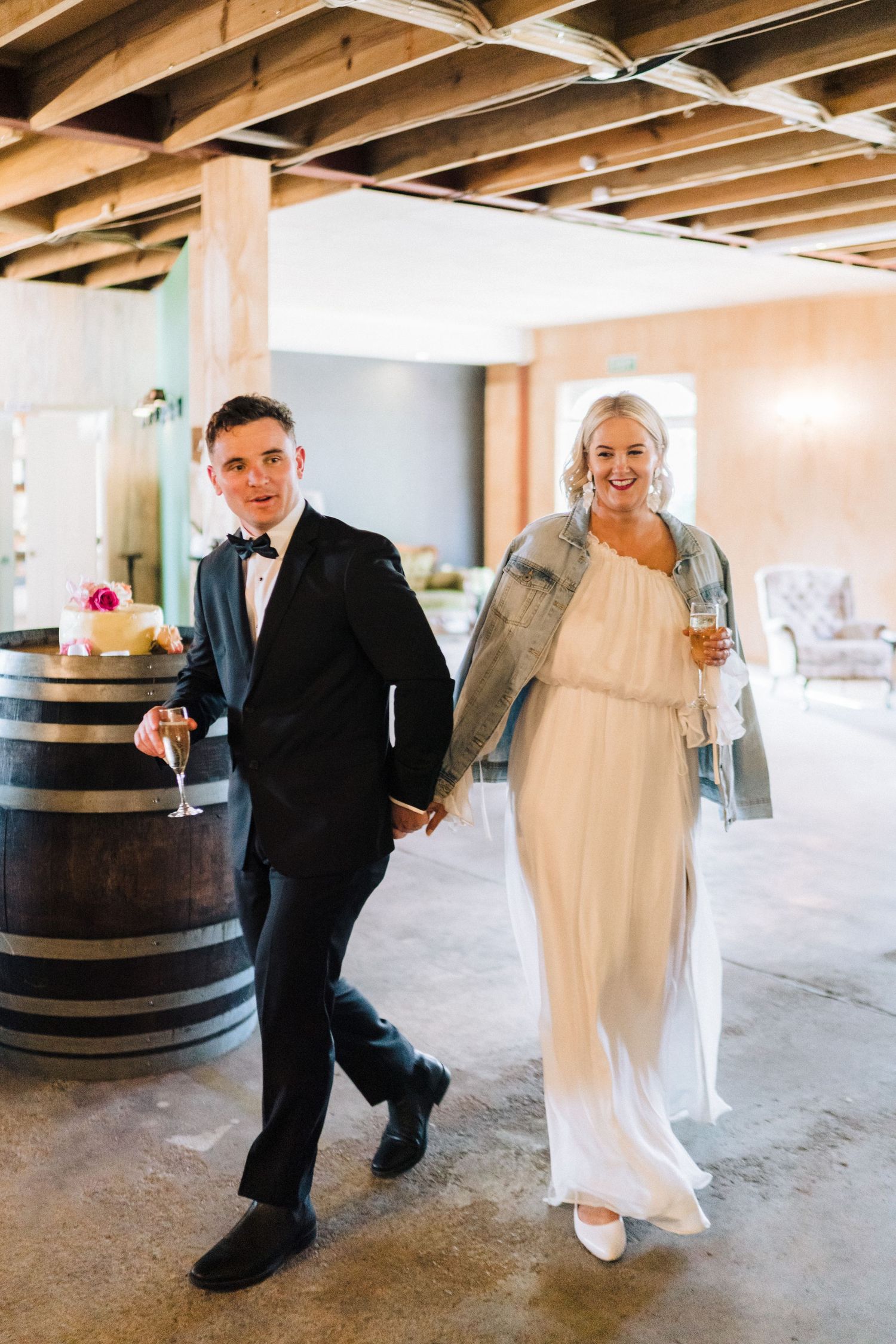 Wedding couple walking together in industrial venue space with wooden barrels and exposed ceiling beams.