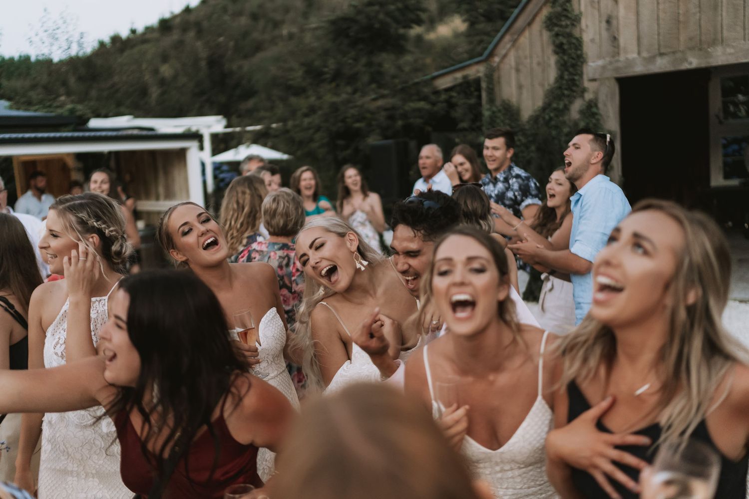 A joyful crowd laughs and celebrates together at an outdoor party on a sunny day.