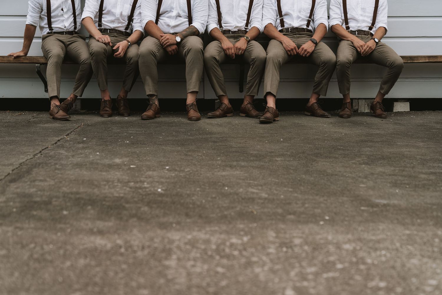 A row of legs and feet dangling off a white painted porch ledge, showing a casual summer gathering.
