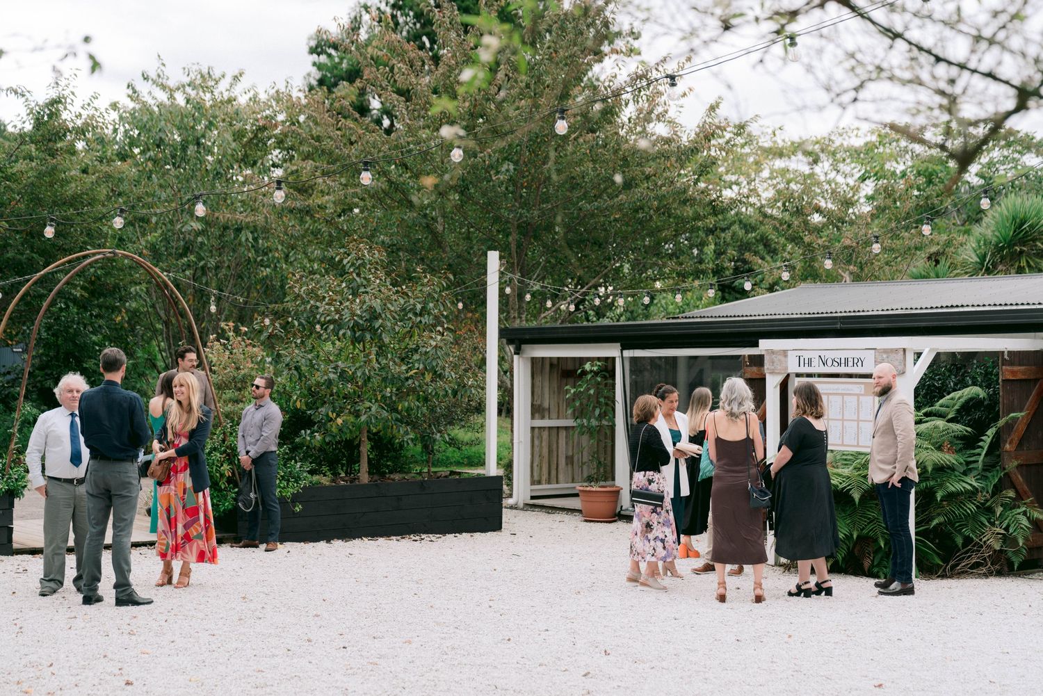 Wedding guests gather in a serene outdoor garden setting on wooden benches arranged in rows.