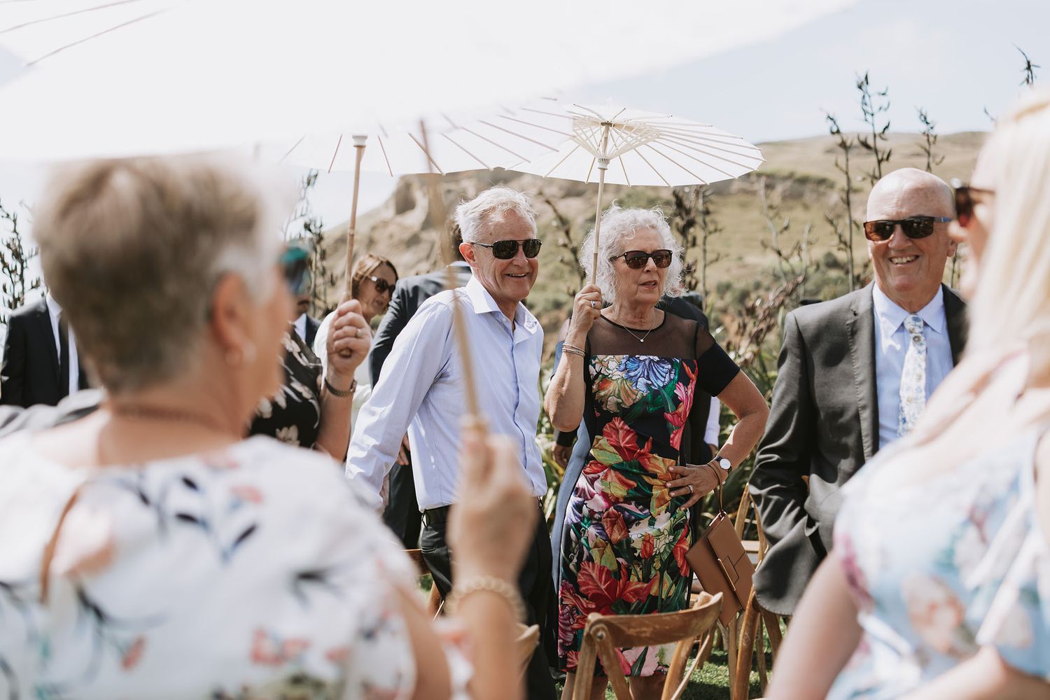 Wedding guests in sunglasses mingle at an outdoor summer celebration under a tent canopy.