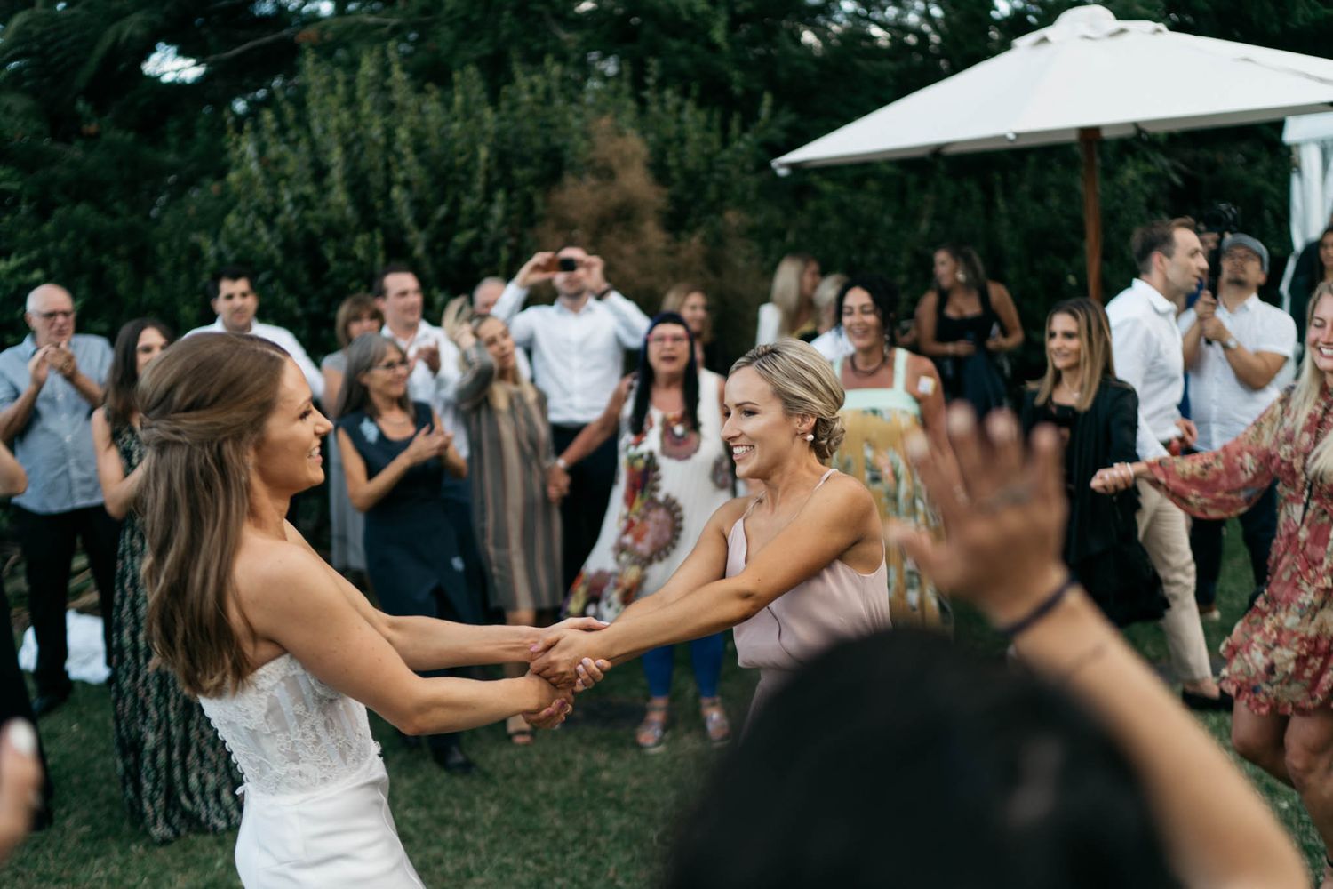 Joyous celebration at an outdoor garden wedding reception as people dance and celebrate under a white umbrella.