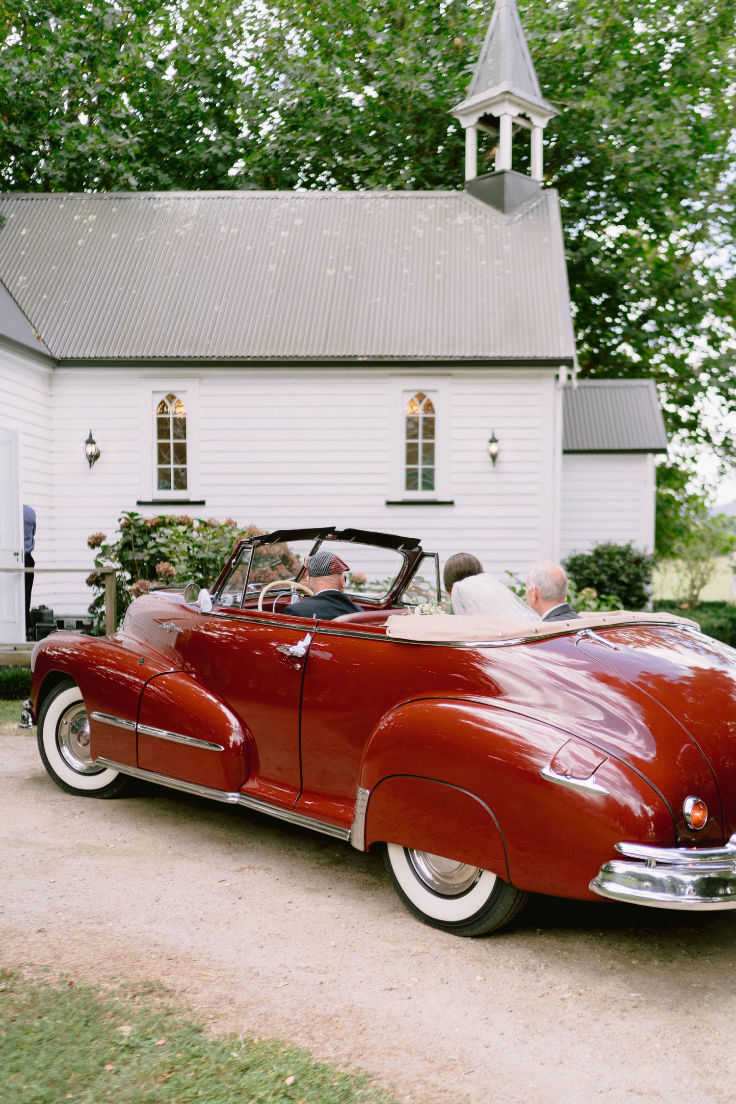 A classic red vintage convertible car parked in front of a white church building.