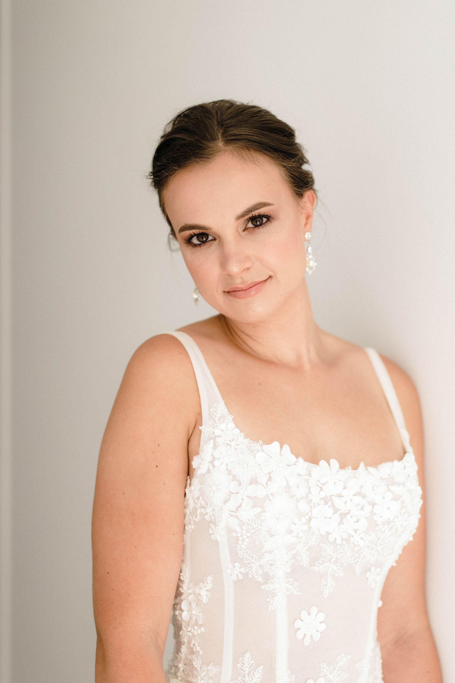 Portrait of someone wearing an elegant white lace wedding dress with delicate floral details.